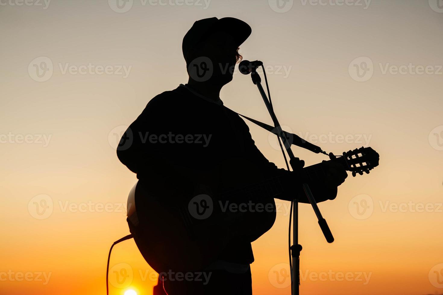 silhouette d'un homme jouant de la guitare et chantant dans un microphone au coucher du soleil photo
