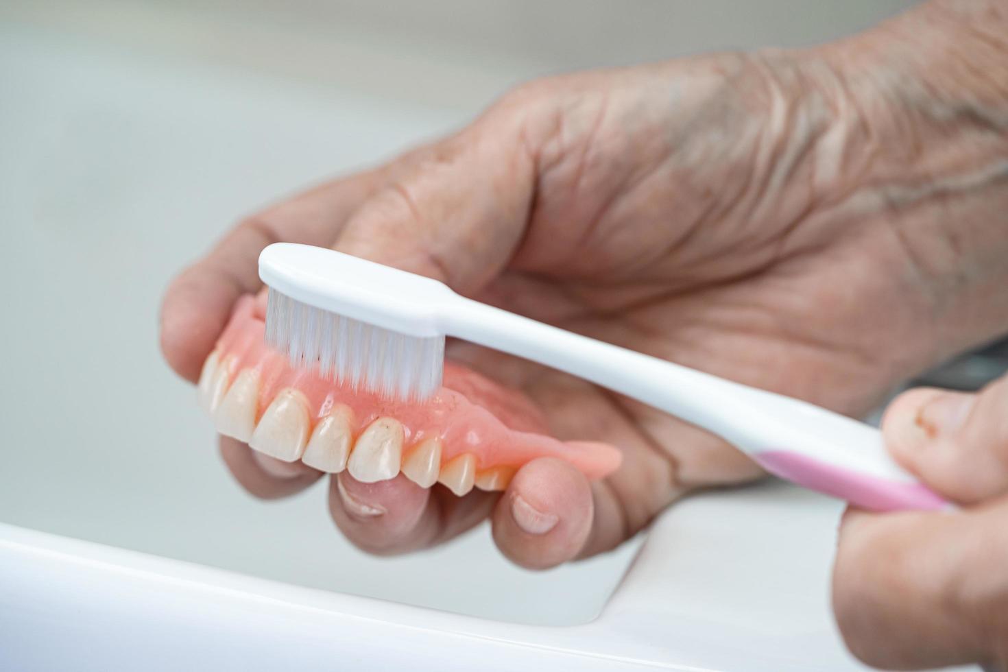 Une patiente asiatique âgée ou âgée utilise une brosse à dents pour nettoyer la prothèse partielle des dents de remplacement. photo