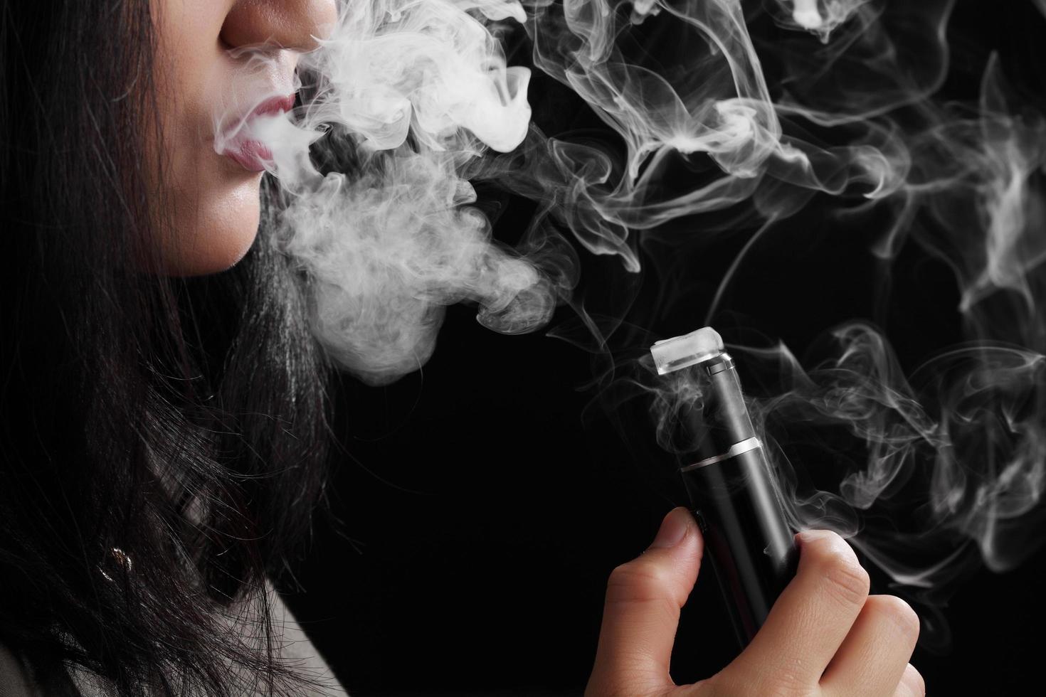 Close up young woman smoking e-cigarette sur fond noir photo