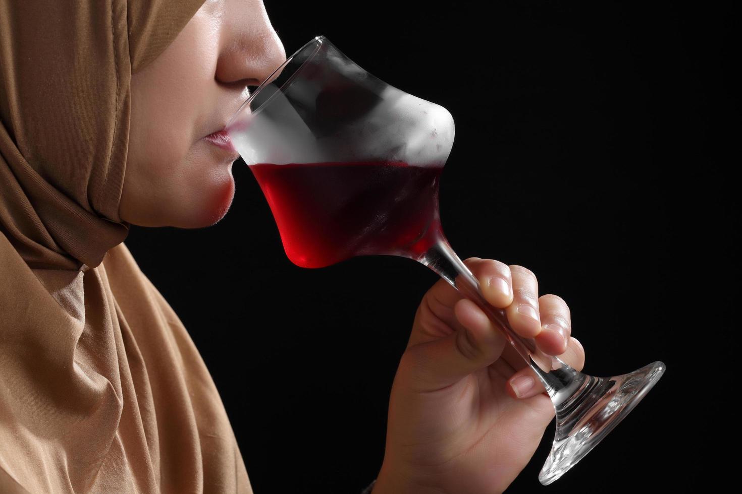 Close up femme musulmane dans un hijab boire du vin rouge sur fond noir photo
