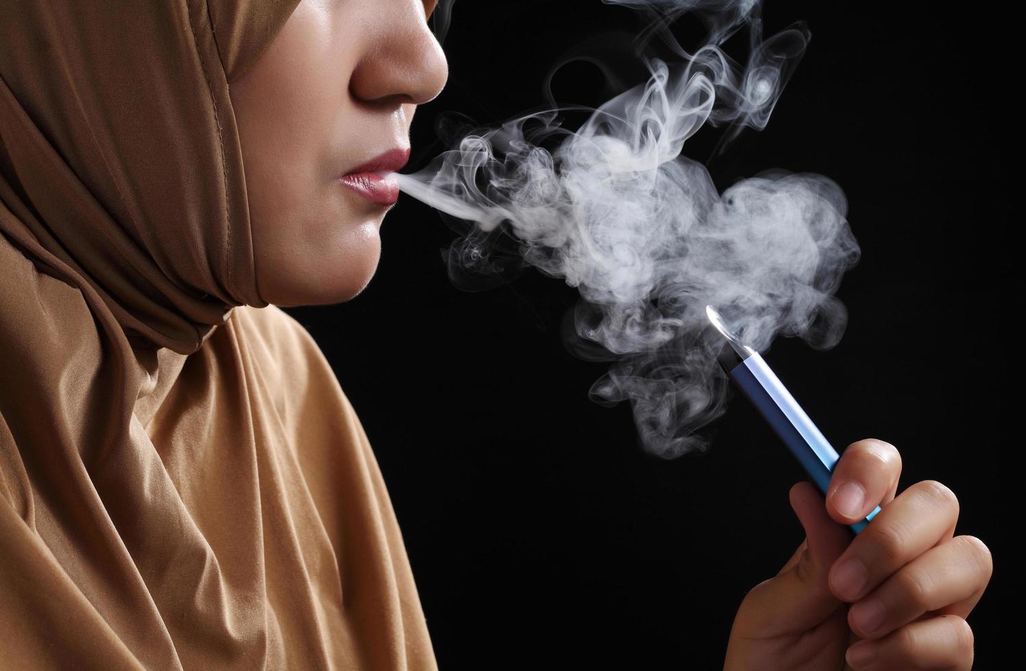 Close up jeune femme musulmane fumer e-cigarette sur fond noir photo