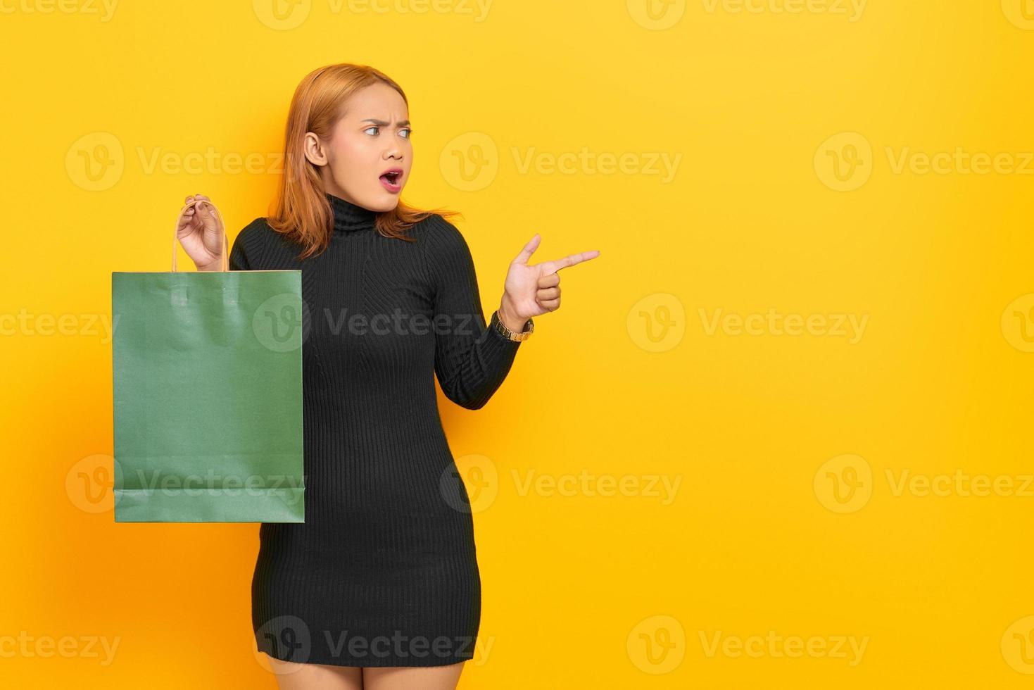 surpris, jeune femme asiatique, tenue, sacs provisions, et, doigt pointé, à, copie, espace, isolé, sur, fond jaune photo