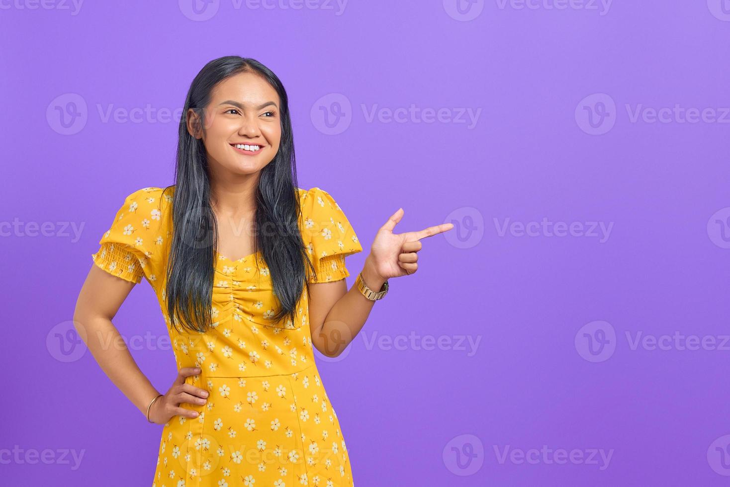 Portrait de jeune femme asiatique souriante pointant le doigt sur l'espace de copie sur fond violet photo