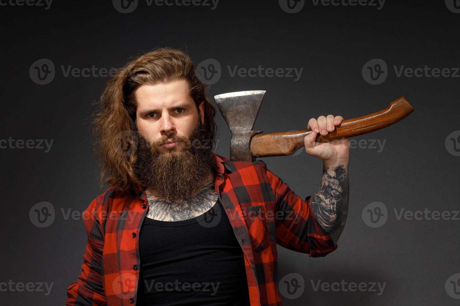 bel homme aux cheveux longs avec une hache dans les mains sur un fond de studio sombre photo