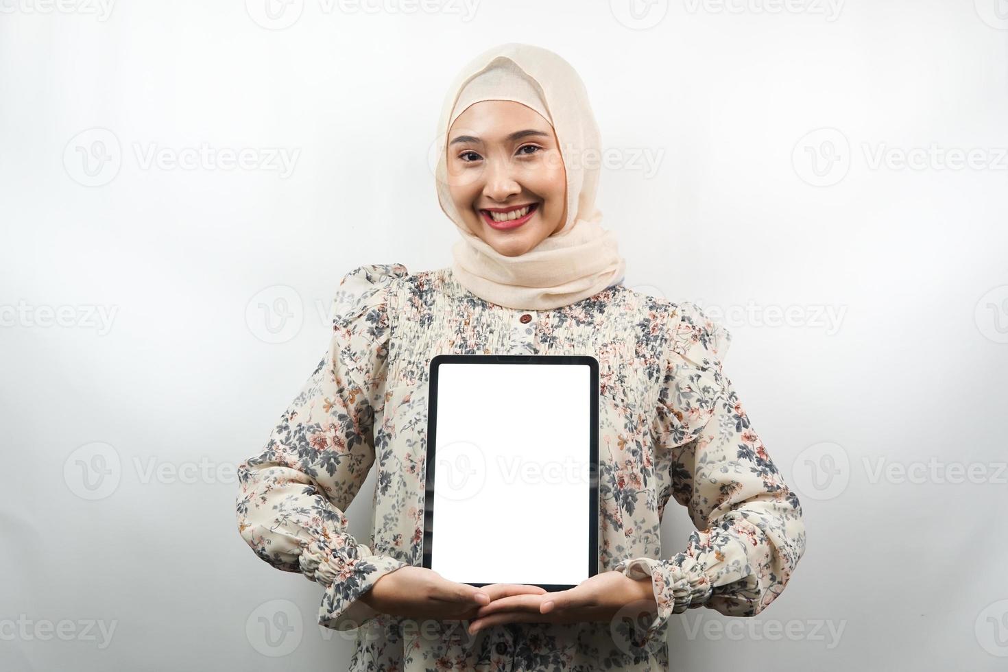 belle jeune femme musulmane asiatique souriante, excitée et joyeuse tenant une tablette avec un écran blanc ou vide, faisant la promotion de l'application, faisant la promotion du produit, présentant quelque chose, isolée sur fond blanc photo