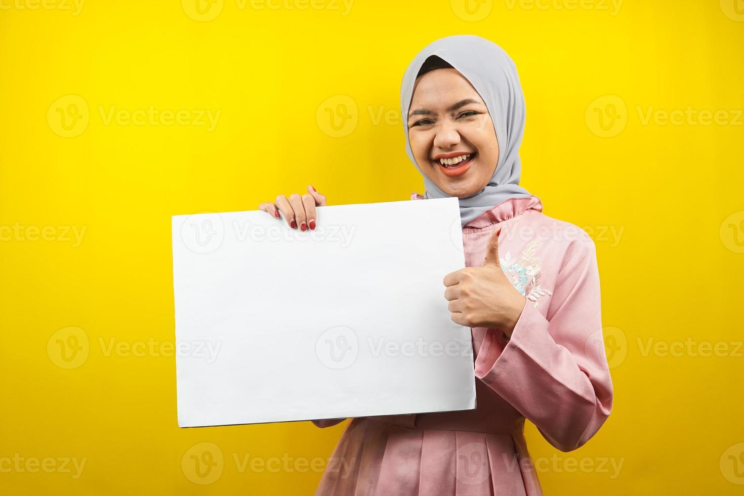 jolie jeune femme musulmane joyeuse tenant une bannière vide vierge, une pancarte, un tableau blanc, un panneau vierge, un panneau publicitaire blanc, présentant quelque chose dans l'espace de copie, promotion photo