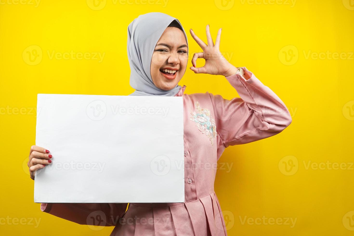 jolie jeune femme musulmane joyeuse tenant une bannière vide vierge, une pancarte, un tableau blanc, un panneau vierge, un panneau publicitaire blanc, présentant quelque chose dans l'espace de copie, promotion photo