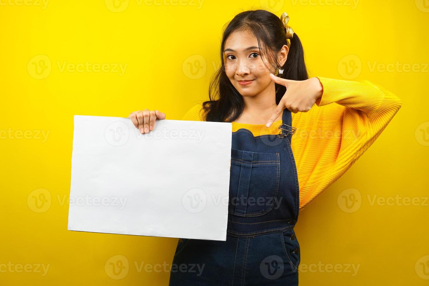 jolie et mignonne jeune femme joyeuse tenant une bannière vide vierge, une pancarte, un tableau blanc, un panneau vierge, un panneau publicitaire blanc, présentant quelque chose dans l'espace de copie, promotion photo