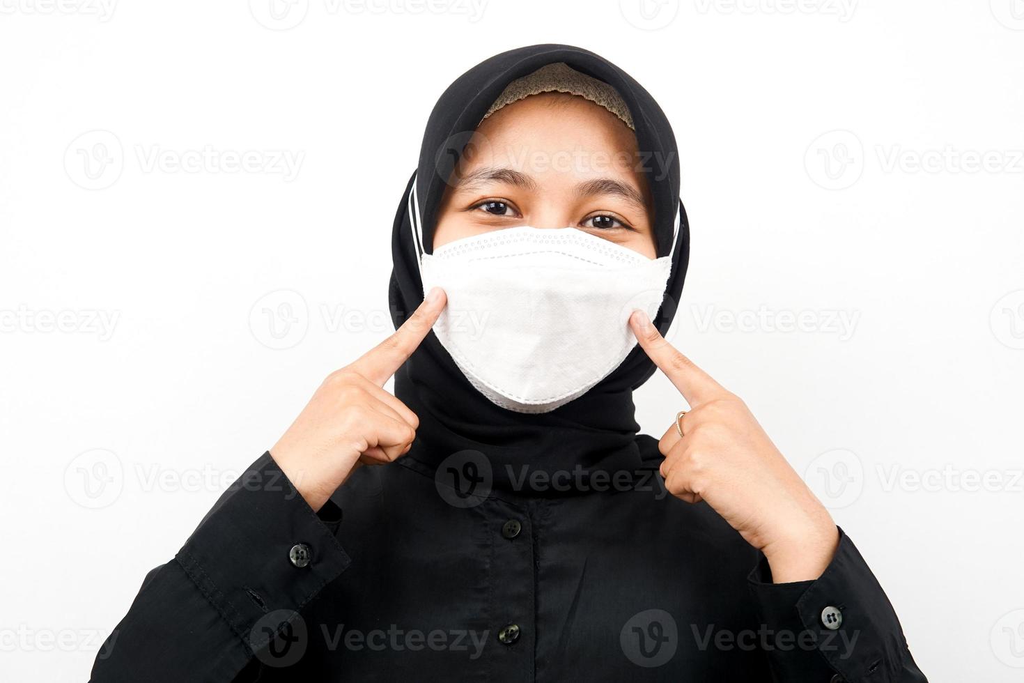 gros plan d'une belle jeune femme musulmane portant un masque blanc, main pointant sur le masque, corona, covid-19, isolé photo