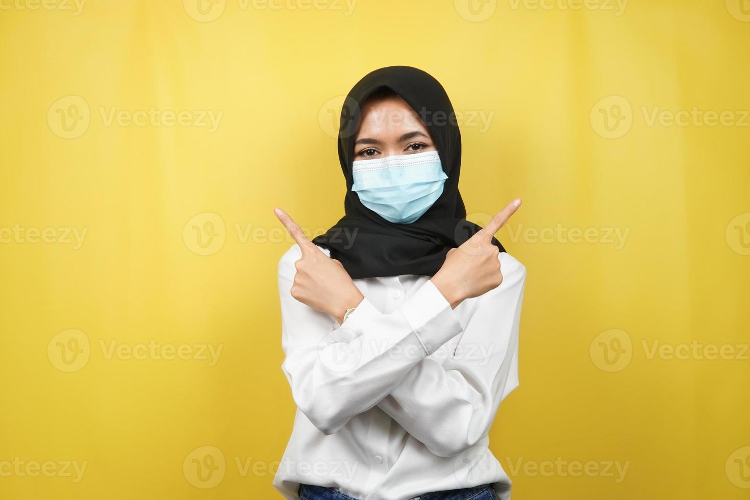 femme musulmane portant un masque médical, main pointant vers un espace vide, main pointant vers le haut présentant quelque chose, isolée sur fond jaune photo