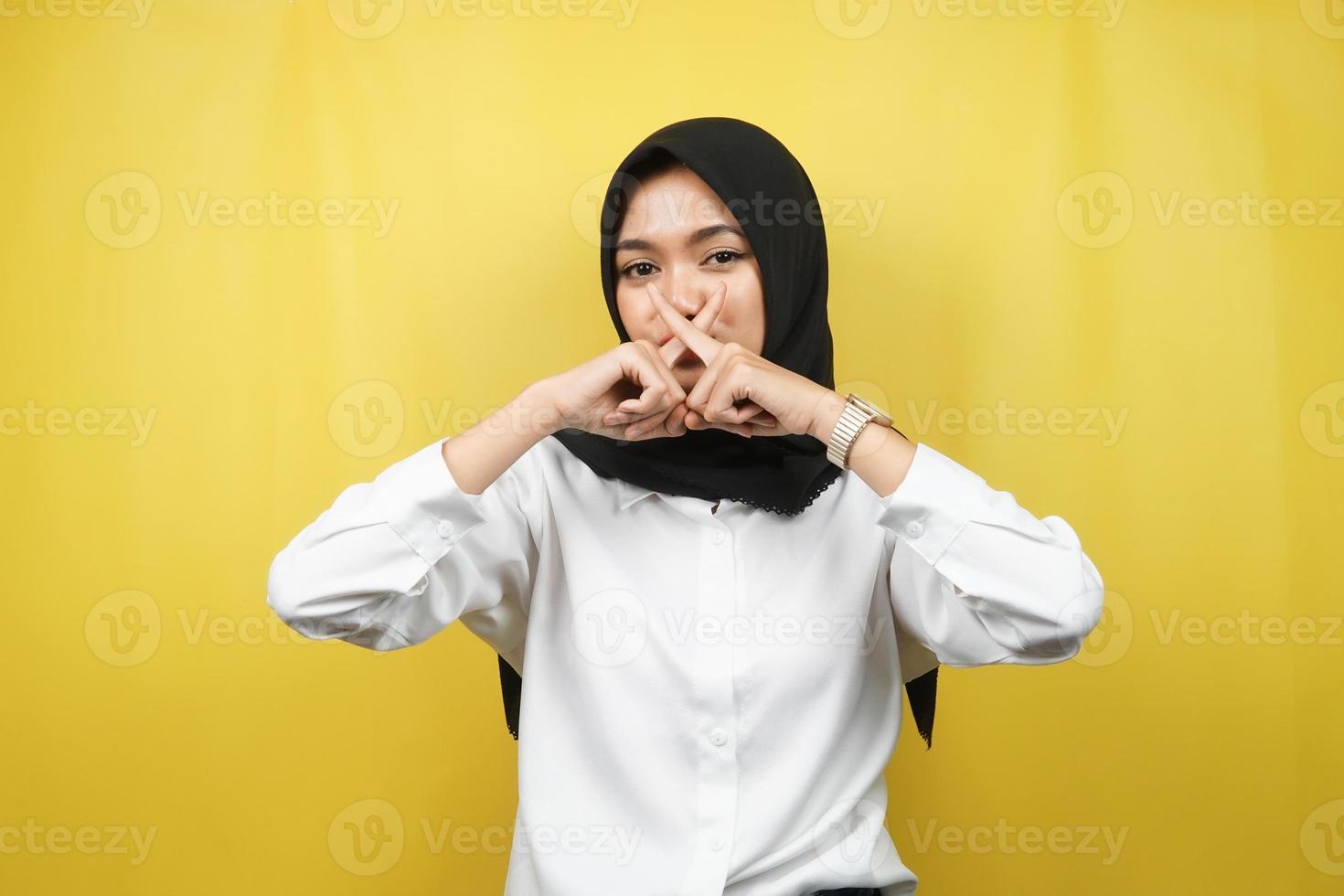 belle jeune femme musulmane asiatique avec le doigt sur la bouche, disant de se taire, de ne pas faire de bruit, de baisser la voix, de ne pas parler, isolée sur fond jaune photo