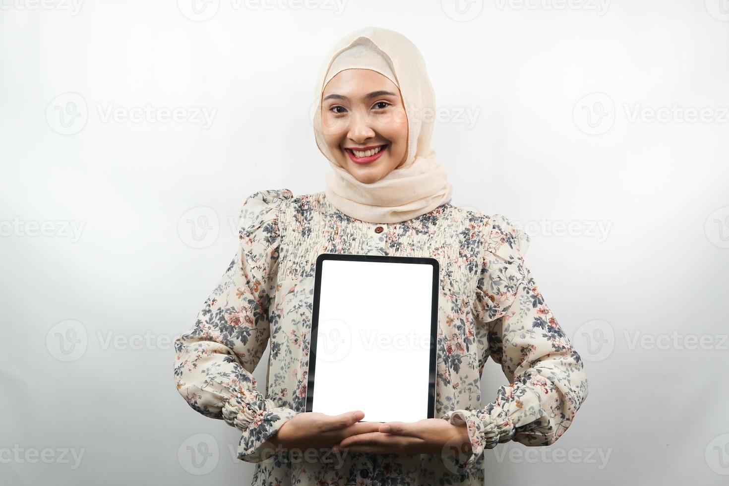 belle jeune femme musulmane asiatique souriante, excitée et joyeuse tenant une tablette avec un écran blanc ou vide, faisant la promotion de l'application, faisant la promotion du produit, présentant quelque chose, isolée sur fond blanc photo