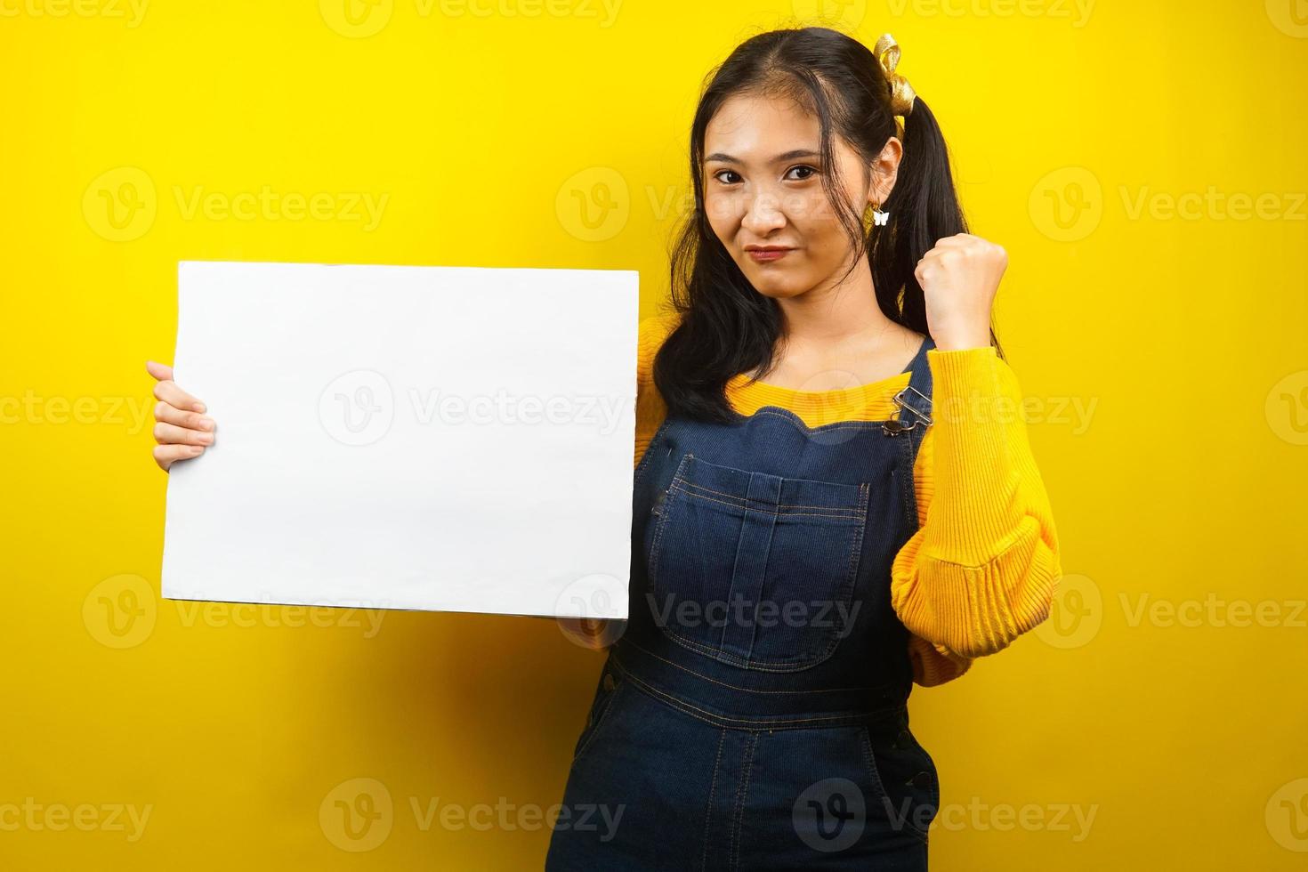 jolie et mignonne jeune femme joyeuse tenant une bannière vide vierge, une pancarte, un tableau blanc, un panneau vierge, un panneau publicitaire blanc, présentant quelque chose dans l'espace de copie, promotion photo