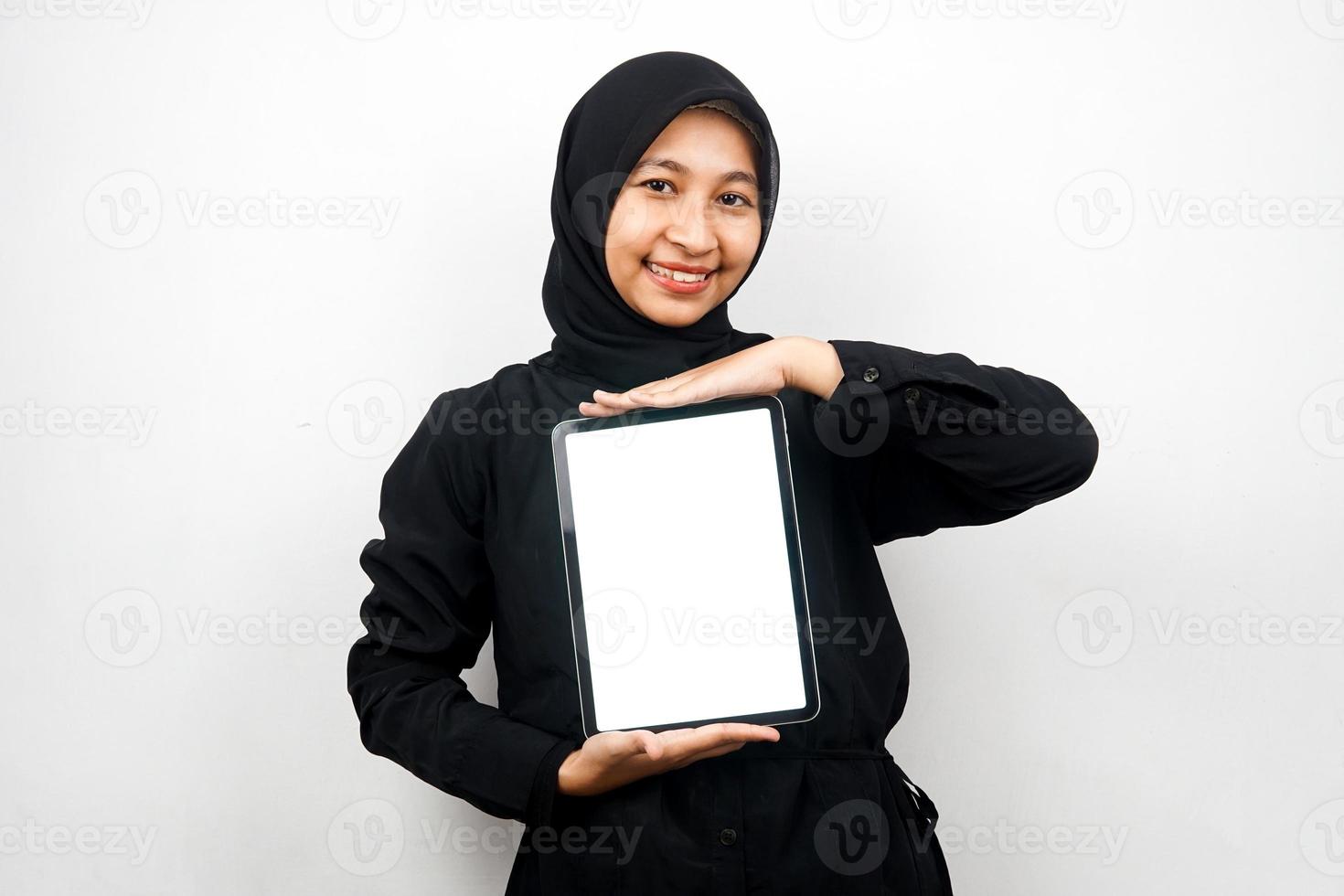 belle jeune femme musulmane asiatique souriante, tenant une tablette à la main avec un écran blanc ou blanc, faisant la promotion de l'application, faisant la promotion du produit, présentant quelque chose, excité et joyeux, isolé sur fond blanc photo