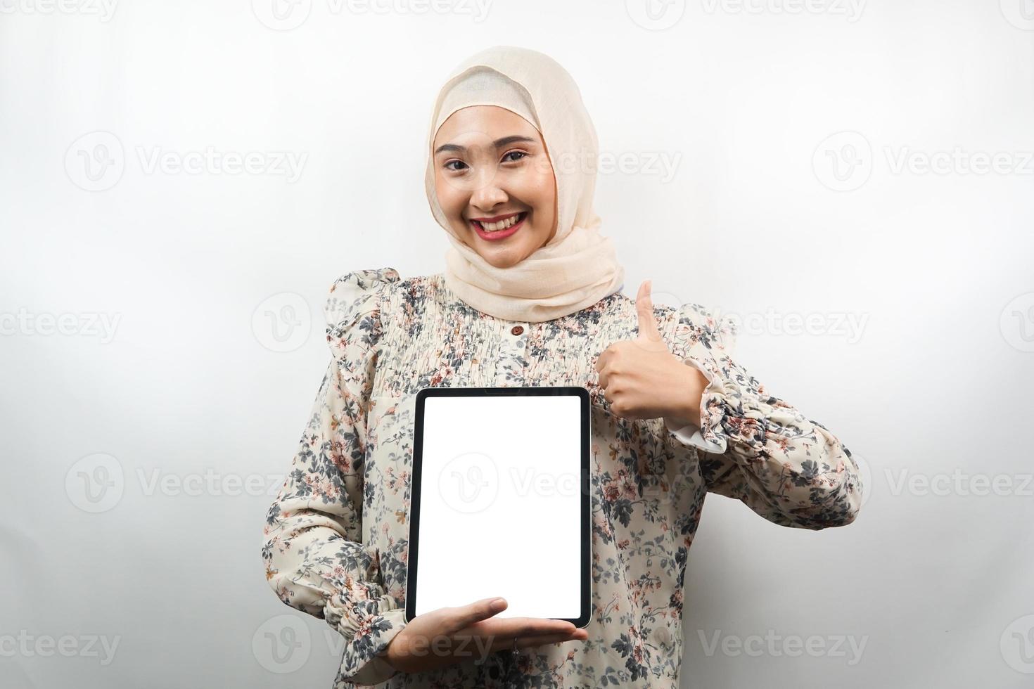 belle jeune femme musulmane asiatique souriante, excitée et joyeuse tenant une tablette avec un écran blanc ou vide, faisant la promotion de l'application, faisant la promotion du produit, présentant quelque chose, isolée sur fond blanc photo