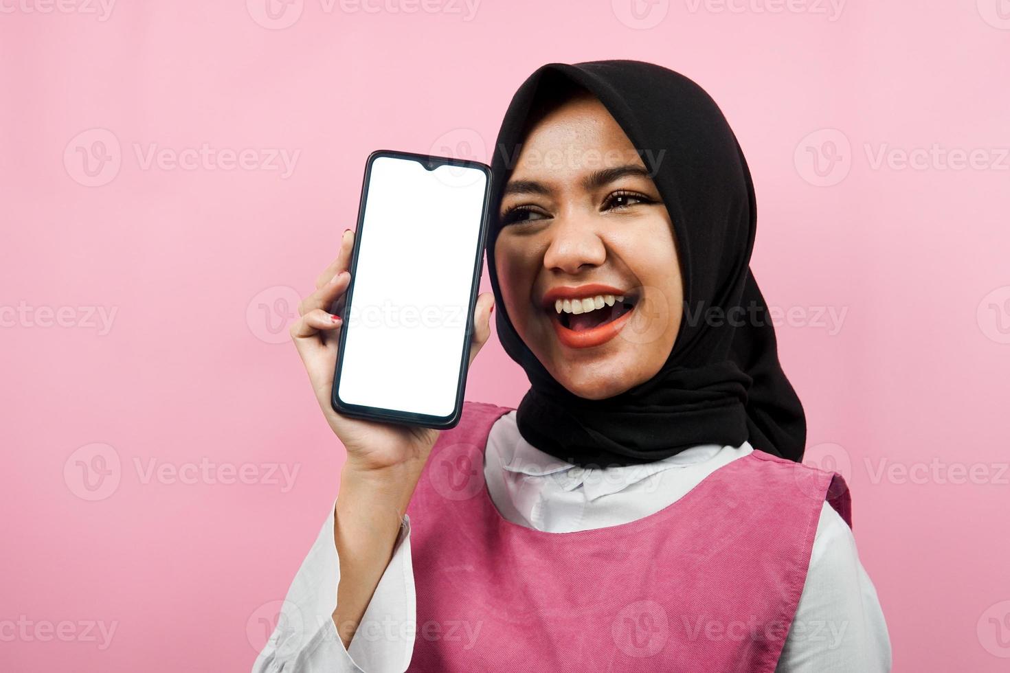 gros plan d'une jeune femme musulmane belle et joyeuse tenant un smartphone avec écran blanc ou vierge, faisant la promotion de l'application, faisant la promotion de quelque chose, isolé, concept publicitaire photo