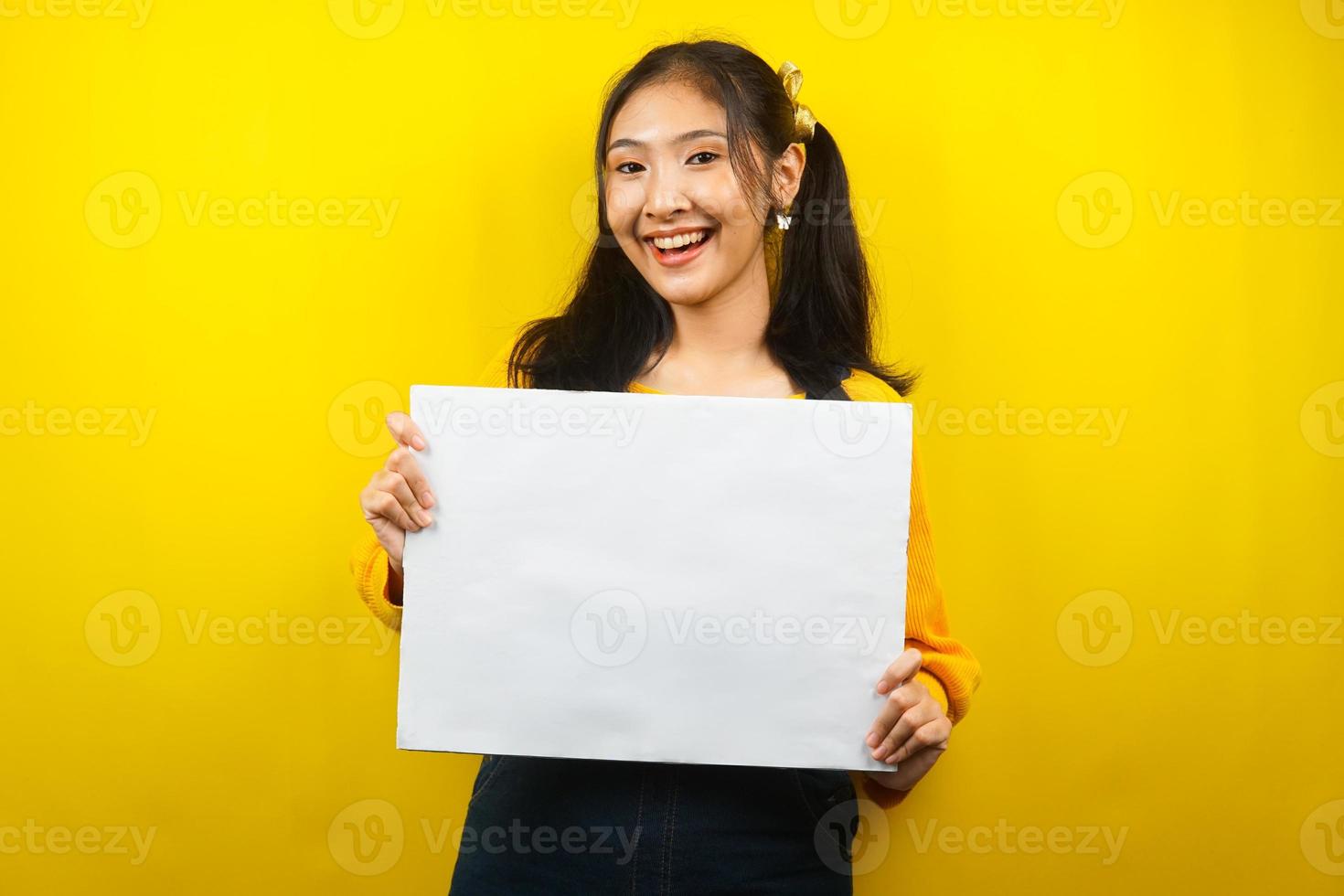 jolie et mignonne jeune femme joyeuse tenant une bannière vide vierge, une pancarte, un tableau blanc, un panneau vierge, un panneau publicitaire blanc, présentant quelque chose dans l'espace de copie, promotion photo