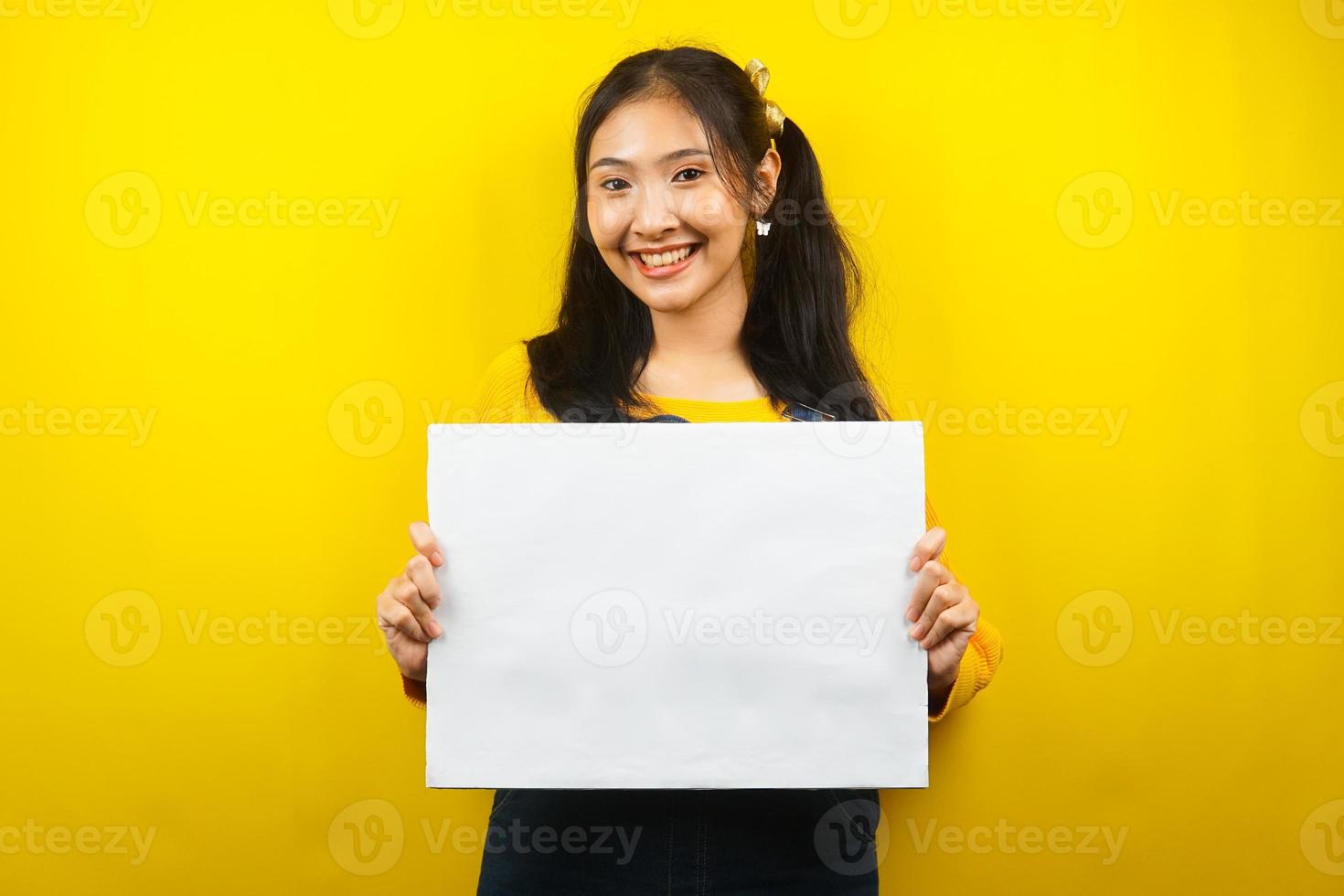 jolie et mignonne jeune femme joyeuse tenant une bannière vide vierge, une pancarte, un tableau blanc, un panneau vierge, un panneau publicitaire blanc, présentant quelque chose dans l'espace de copie, promotion photo