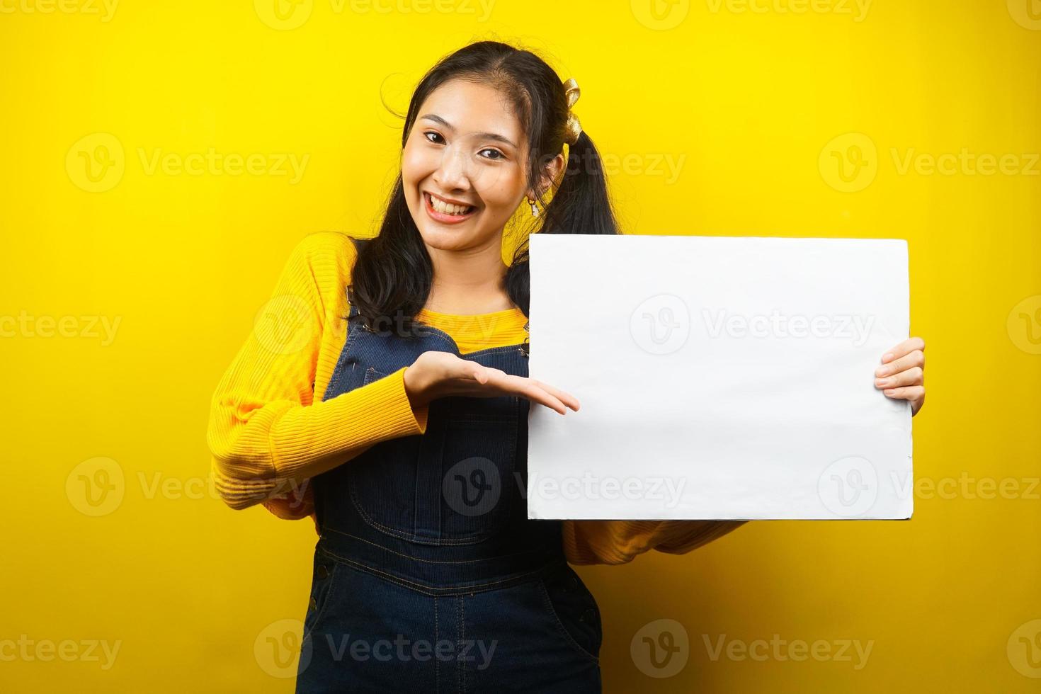 jolie et mignonne jeune femme joyeuse tenant une bannière vide vierge, une pancarte, un tableau blanc, un panneau vierge, un panneau publicitaire blanc, présentant quelque chose dans l'espace de copie, promotion photo