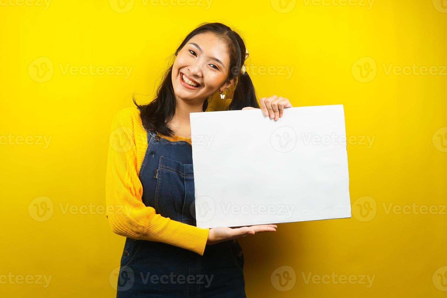 jolie et mignonne jeune femme joyeuse tenant une bannière vide vierge, une pancarte, un tableau blanc, un panneau vierge, un panneau publicitaire blanc, présentant quelque chose dans l'espace de copie, promotion photo