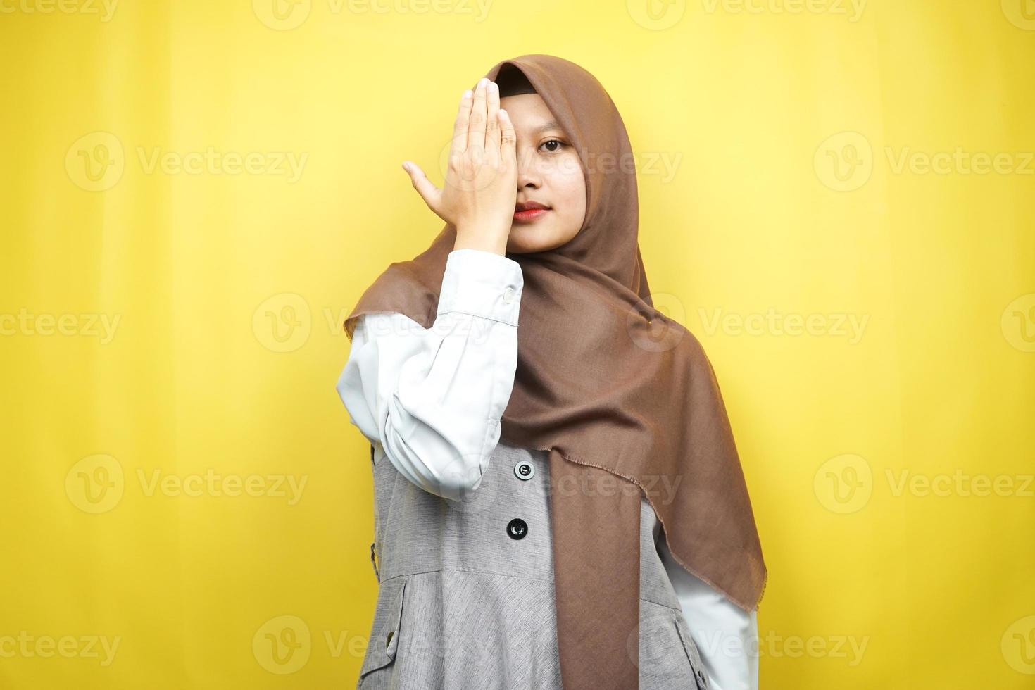 Belle jeune femme musulmane asiatique avec la main couvrant un œil regardant la caméra isolée sur fond jaune photo