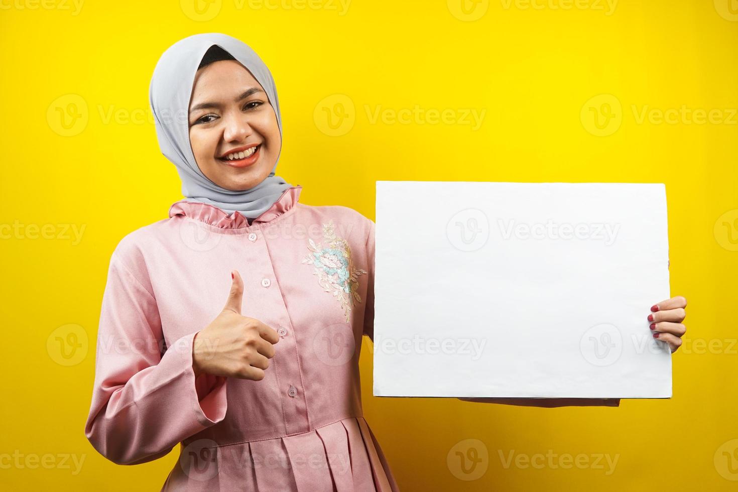 jolie jeune femme musulmane joyeuse tenant une bannière vide vierge, une pancarte, un tableau blanc, un panneau vierge, un panneau publicitaire blanc, présentant quelque chose dans l'espace de copie, promotion photo