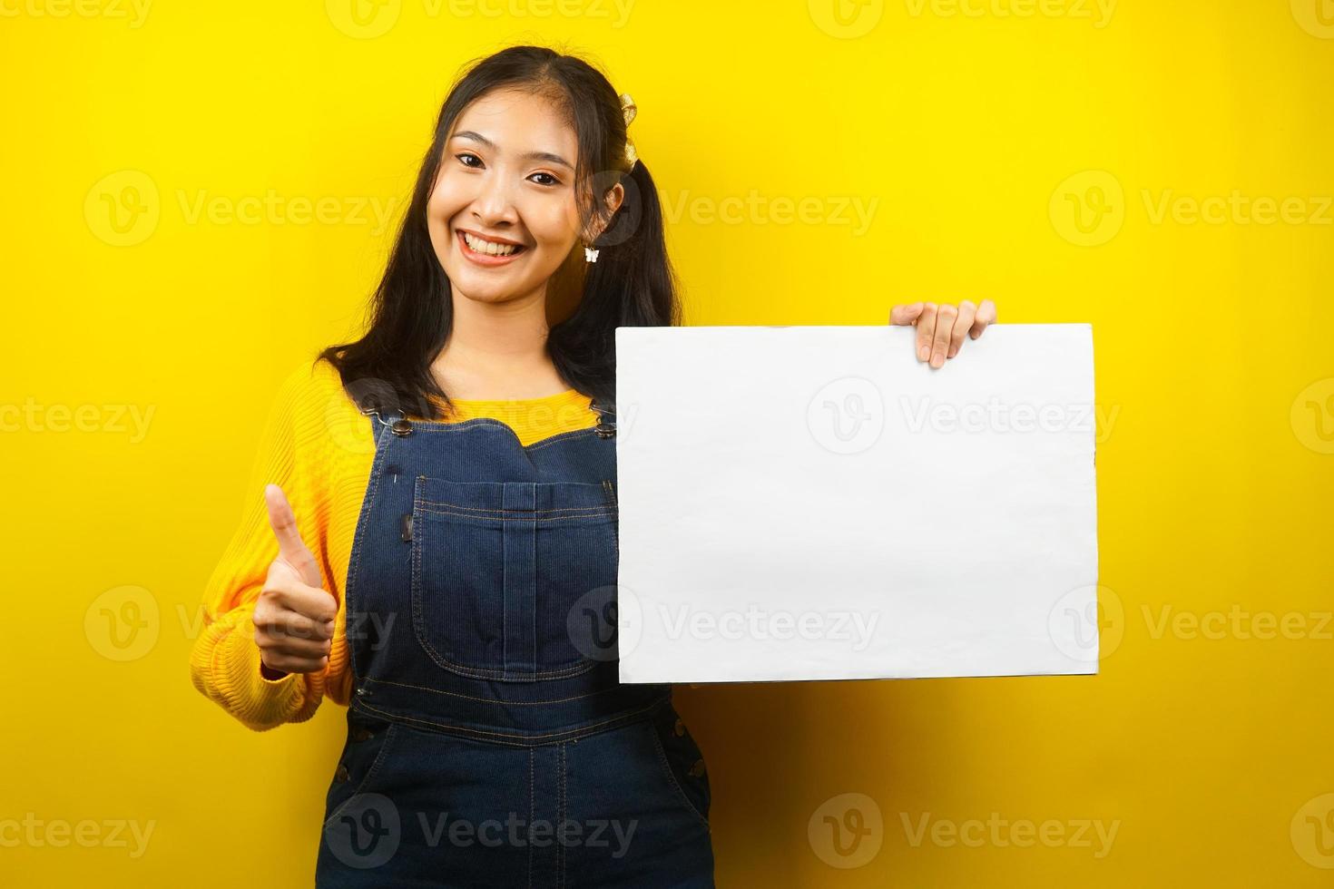 jolie et mignonne jeune femme joyeuse tenant une bannière vide vierge, une pancarte, un tableau blanc, un panneau vierge, un panneau publicitaire blanc, présentant quelque chose dans l'espace de copie, promotion photo