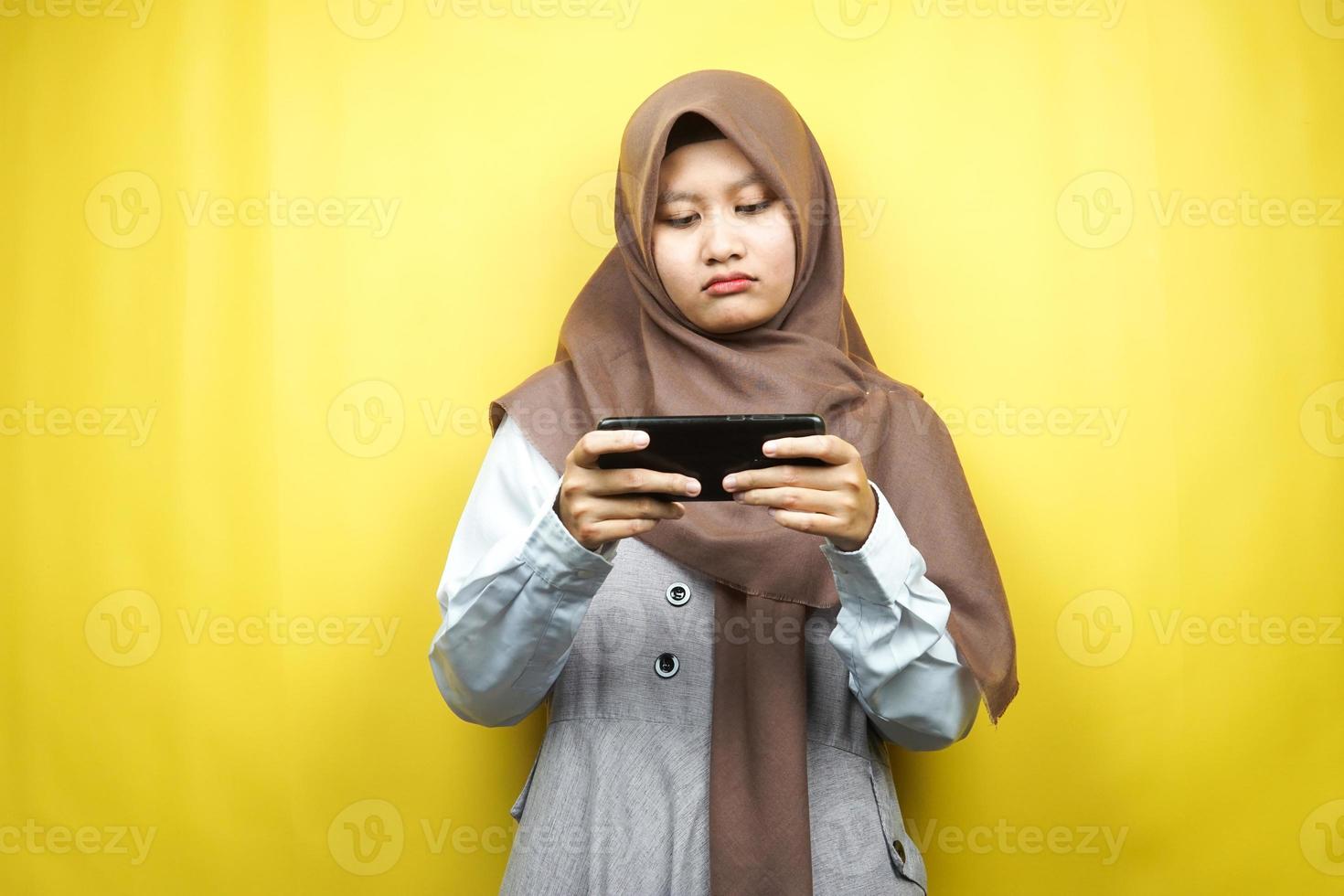 belle jeune femme musulmane asiatique avec une main tenant un smartphone, jouant à un jeu, triste, défaite, malheureuse, isolée sur fond jaune, concept publicitaire photo