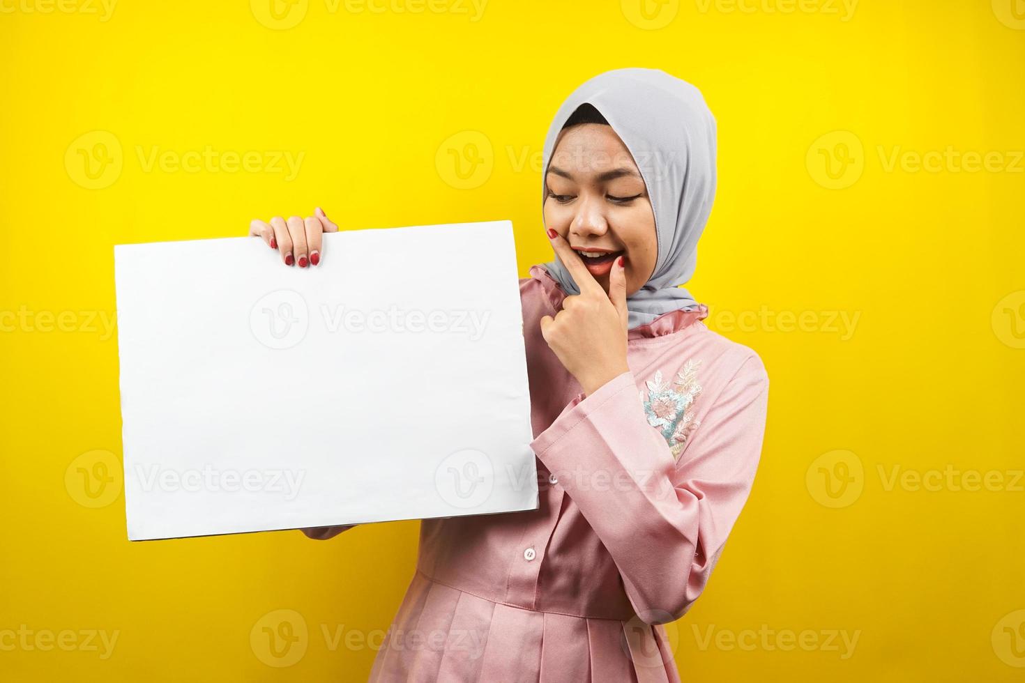 jolie jeune femme musulmane joyeuse tenant une bannière vide vierge, une pancarte, un tableau blanc, un panneau vierge, un panneau publicitaire blanc, présentant quelque chose dans l'espace de copie, promotion photo