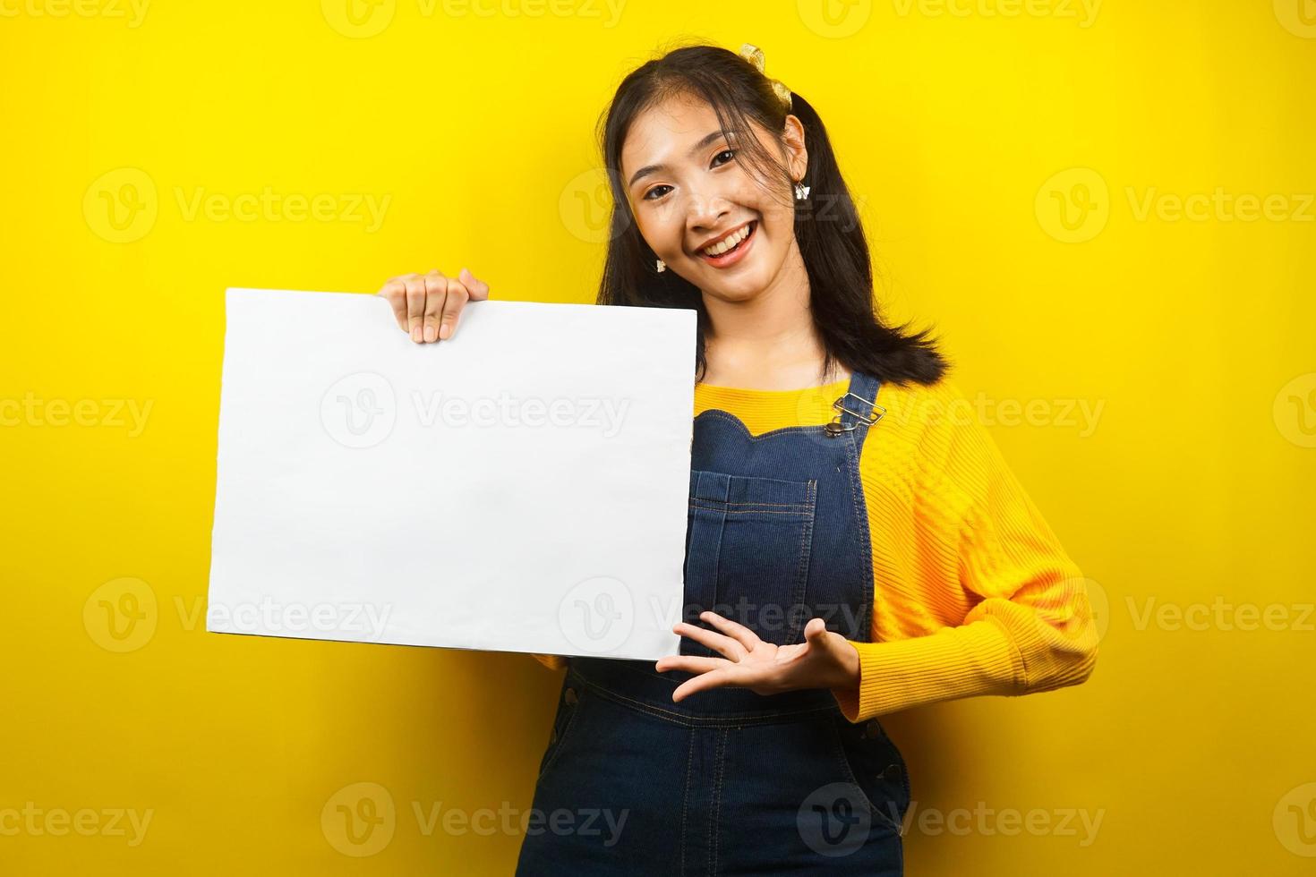 jolie et mignonne jeune femme joyeuse tenant une bannière vide vierge, une pancarte, un tableau blanc, un panneau vierge, un panneau publicitaire blanc, présentant quelque chose dans l'espace de copie, promotion photo