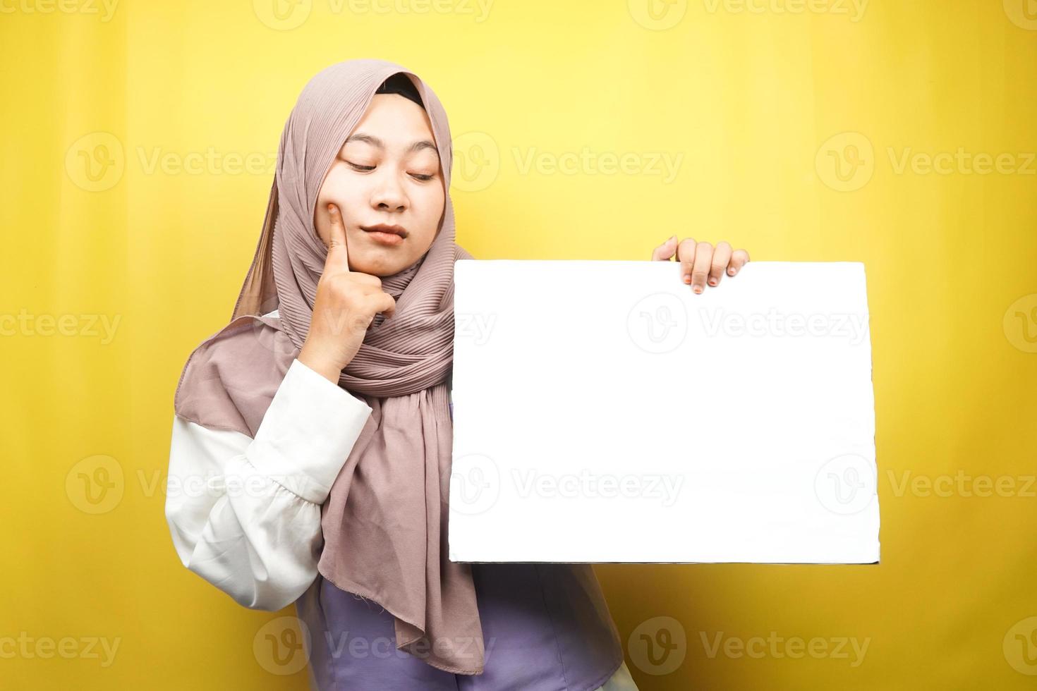 jolie jeune femme musulmane pensant, main tenant une bannière vide vierge, pancarte, tableau blanc, panneau vierge, panneau publicitaire blanc, présentant quelque chose dans l'espace de copie, promotion photo