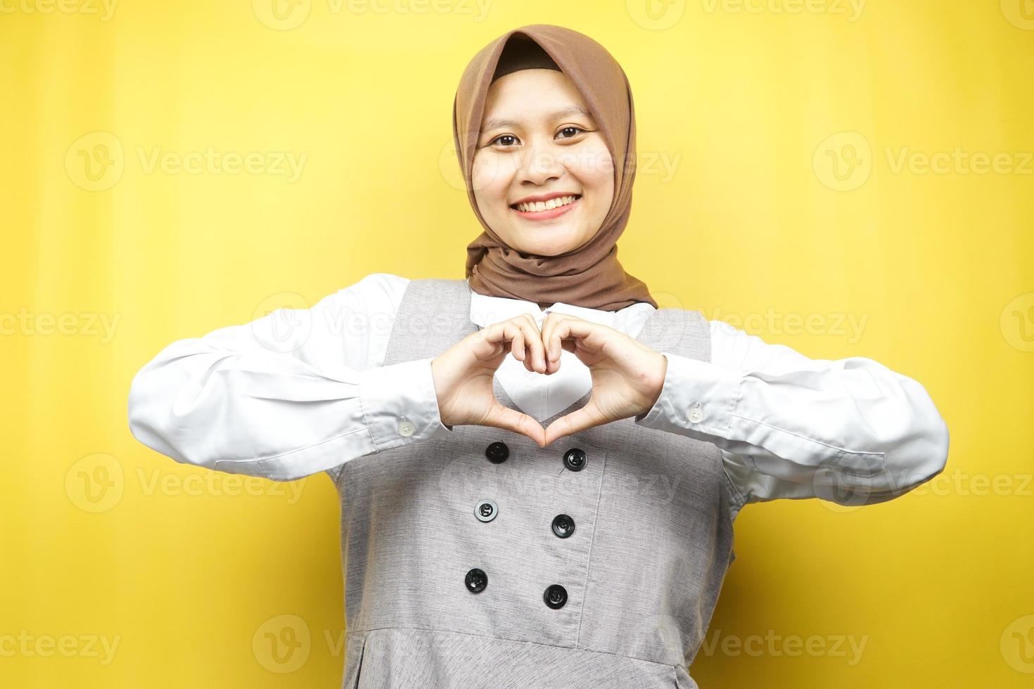 belle jeune femme musulmane asiatique souriante confiante, enthousiaste et joyeuse avec des mains signe d'amour, d'affection, heureuse, sur la poitrine isolée sur fond jaune photo