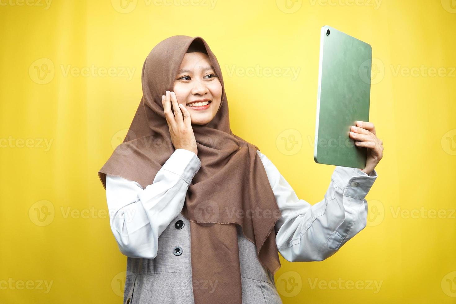 belle jeune femme musulmane asiatique souriante, excitée et joyeuse tenant une tablette, isolée sur fond jaune photo