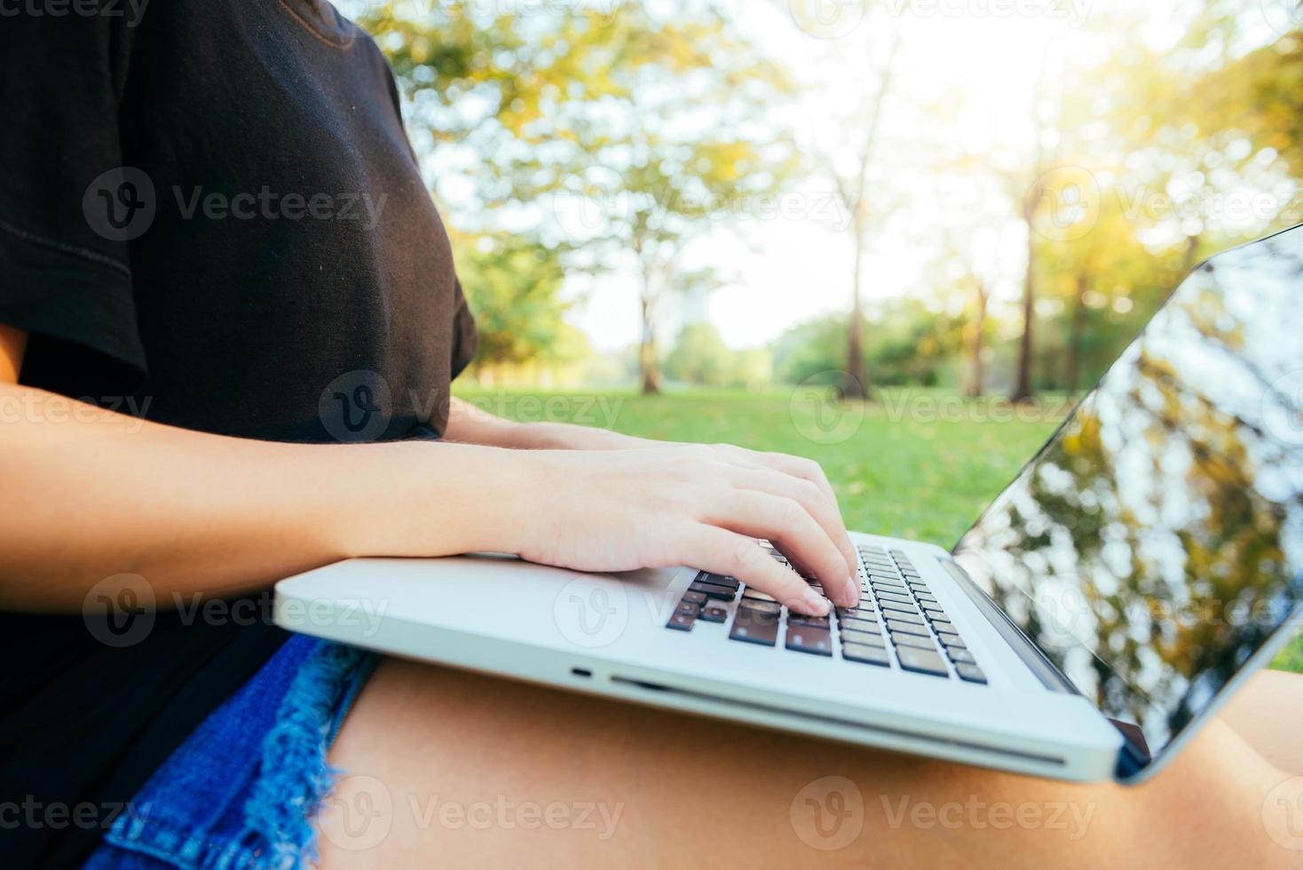 les jambes de la jeune femme asiatique sur l'herbe verte avec un ordinateur portable ouvert. les mains de la fille sur le clavier. concept d'apprentissage à distance. heureux hipster jeune femme asiatique travaillant sur ordinateur portable dans le parc. étudiant étudiant à l'extérieur. photo