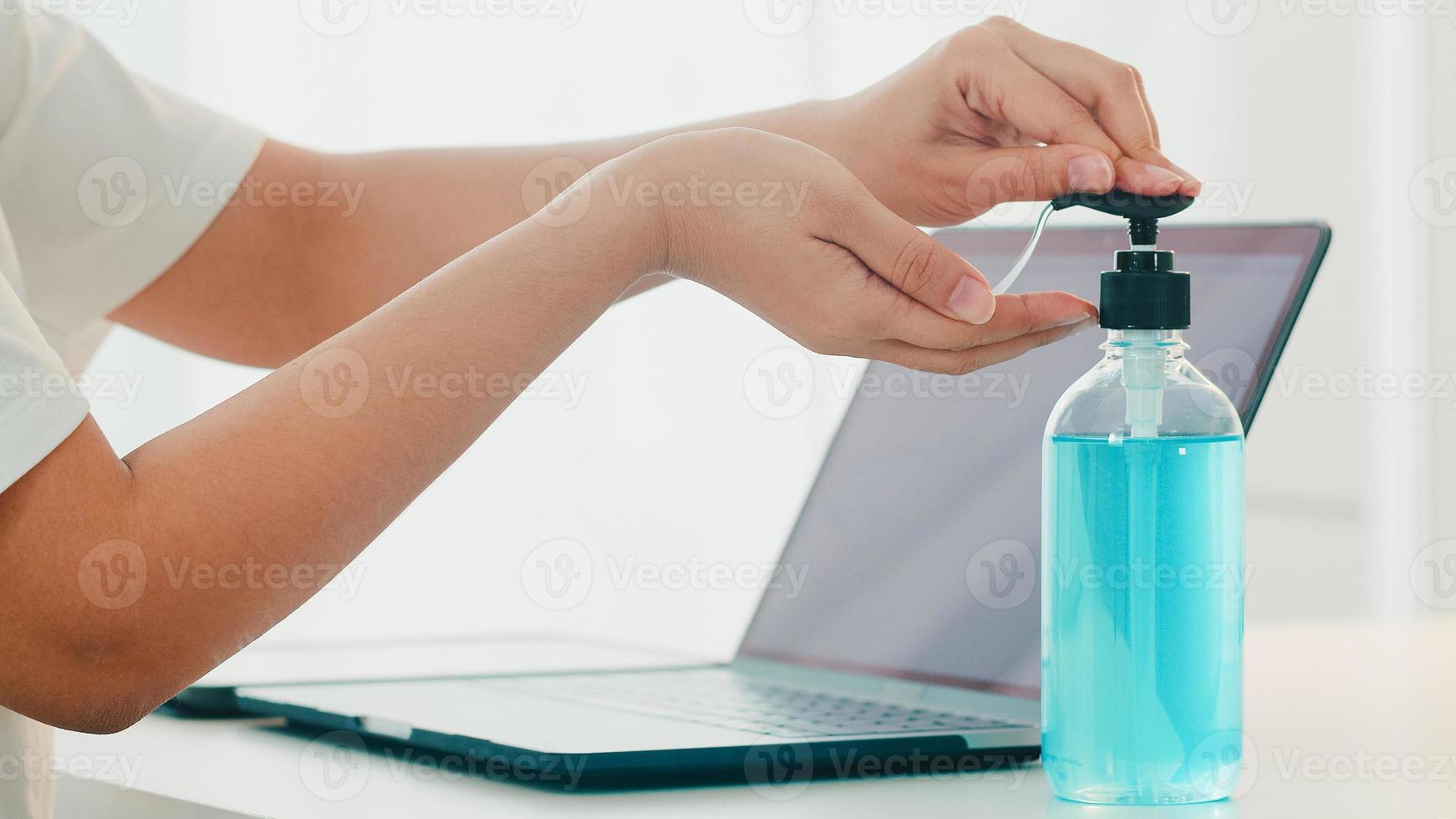 femme asiatique utilisant un désinfectant pour les mains au gel d'alcool se laver les mains avant d'ouvrir l'ordinateur portable pour protéger le coronavirus. les femmes poussent l'alcool à nettoyer pour l'hygiène lorsque la distanciation sociale reste à la maison et le temps d'auto-quarantaine photo