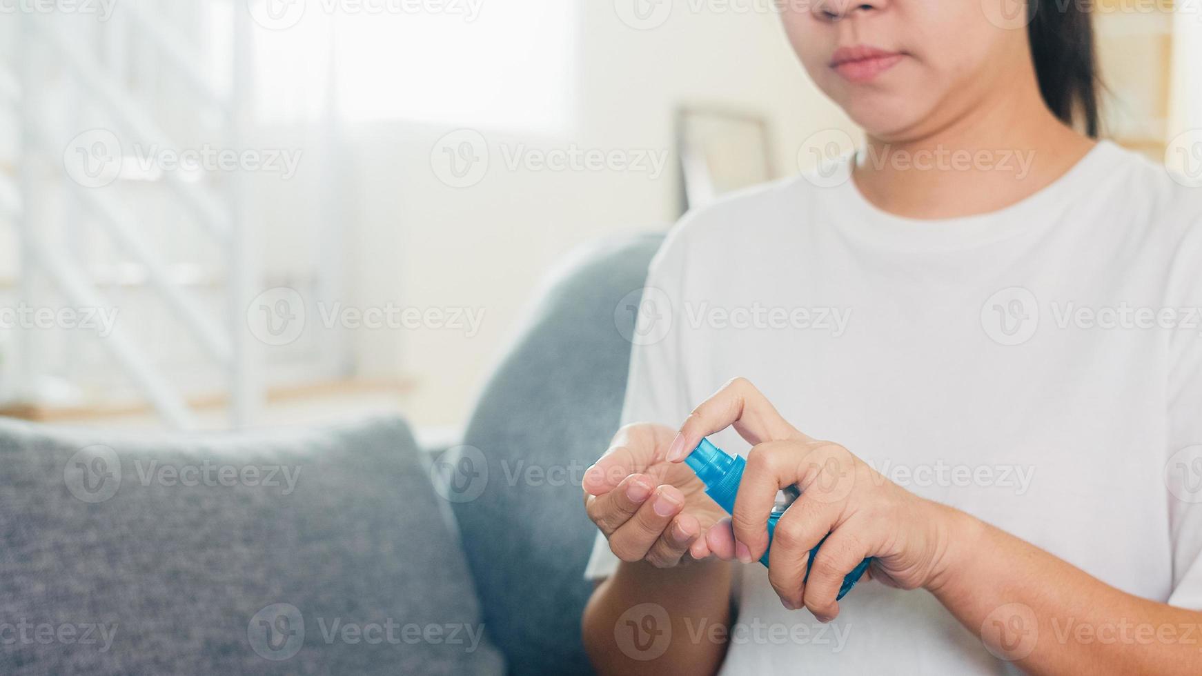 femme asiatique utilisant un désinfectant pour les mains en vaporisateur d'alcool se laver les mains pour protéger le coronavirus. femme assise sur le canapé main propre pour l'hygiène lorsque la distanciation sociale reste à la maison et le temps d'auto-quarantaine. photo