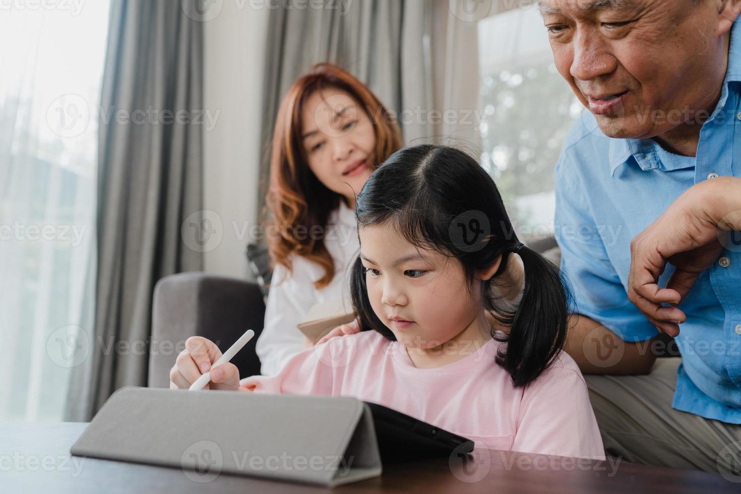 appels vidéo des grands-parents asiatiques et de la petite-fille à la maison. chinois senior, grand-père et grand-mère heureux avec une fille utilisant un appel vidéo sur téléphone portable parlant avec papa et maman allongés dans le salon à la maison. photo