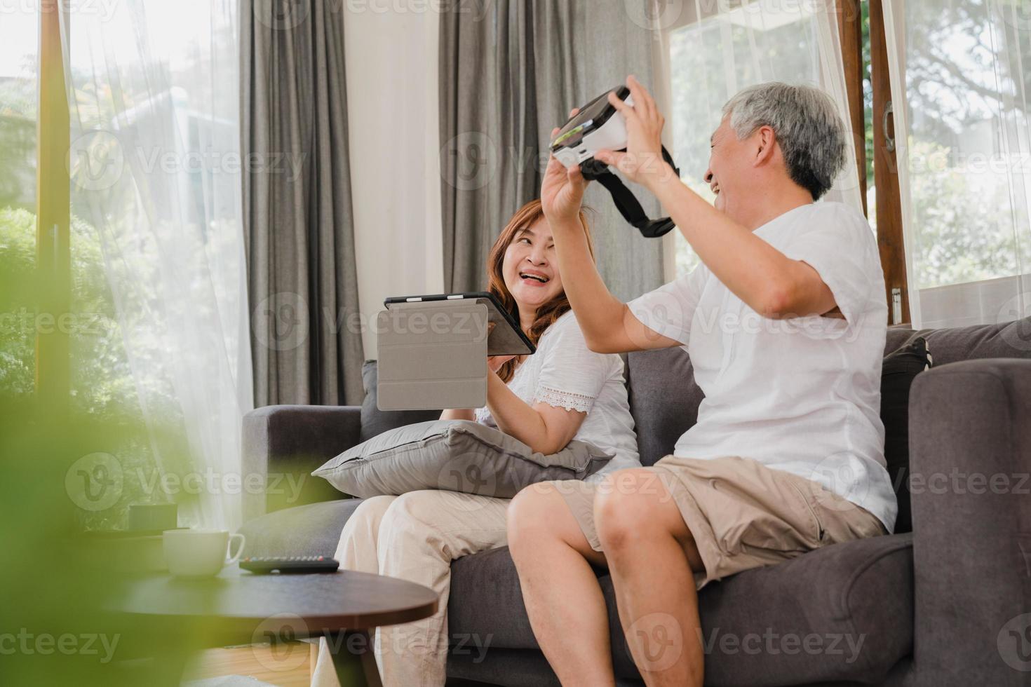 couple de personnes âgées asiatiques utilisant une tablette et un simulateur de réalité virtuelle jouant à des jeux dans le salon, un couple se sentant heureux de passer du temps ensemble allongé sur un canapé à la maison. concept de famille senior de style de vie à la maison. photo