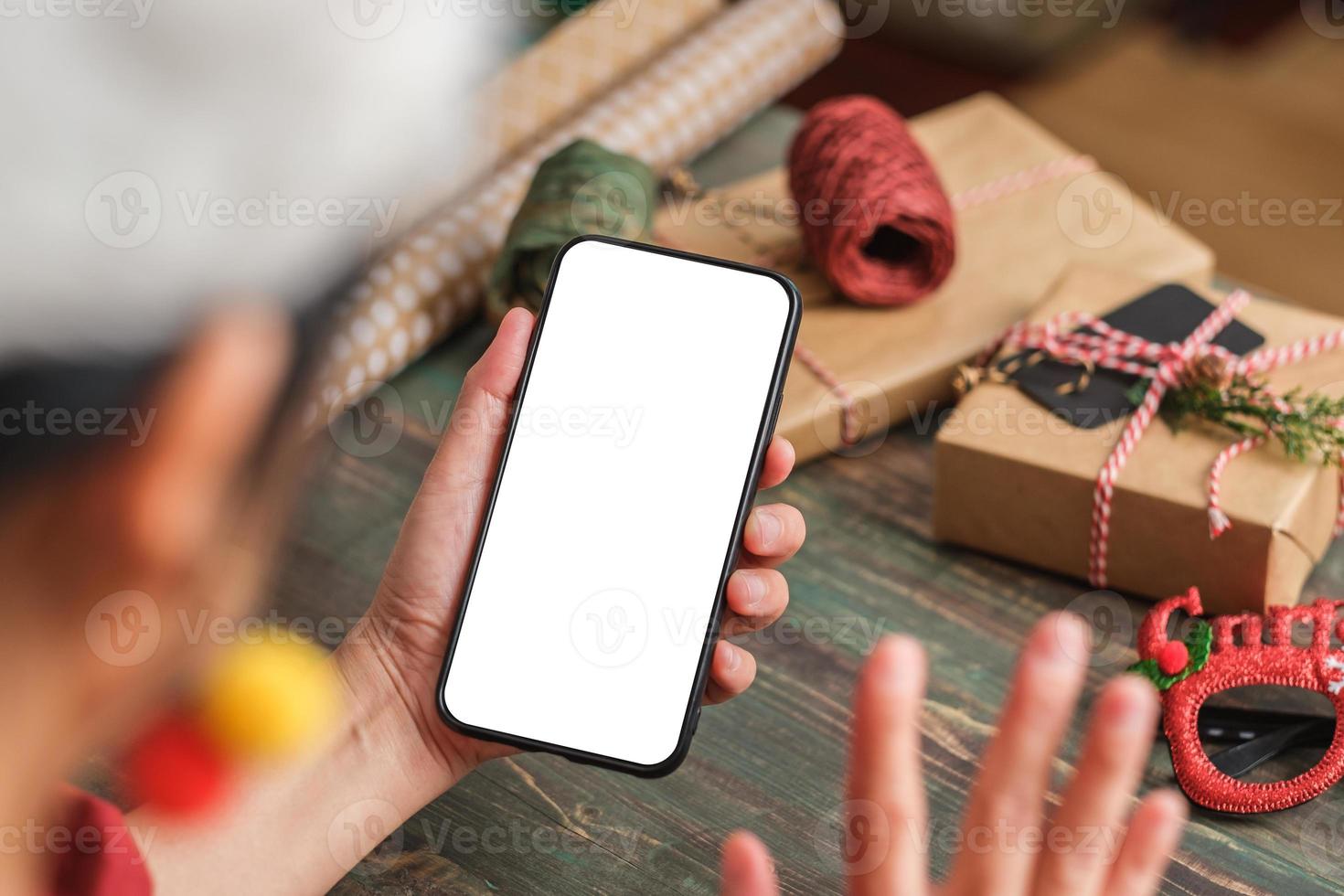 une femme asiatique porte une soirée d'appel vidéo avec un chapeau de père Noël avec des amis avec un téléphone portable sur une table à la maison photo