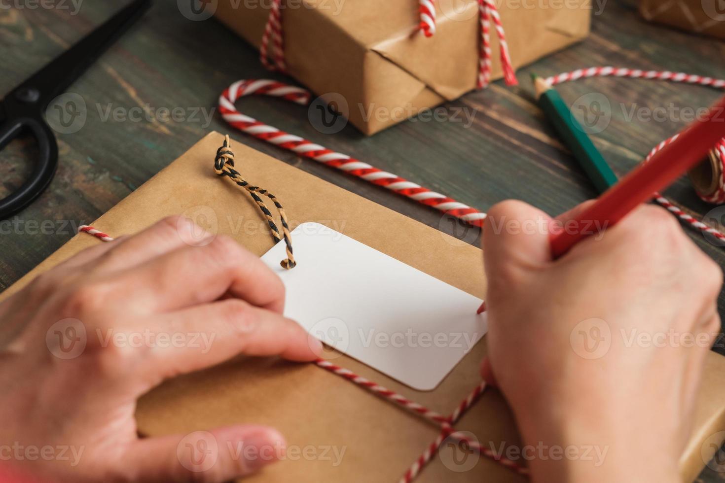 Femme écrivant une étiquette-cadeau et attachez-la au cadeau de Noël sur une table en bois photo