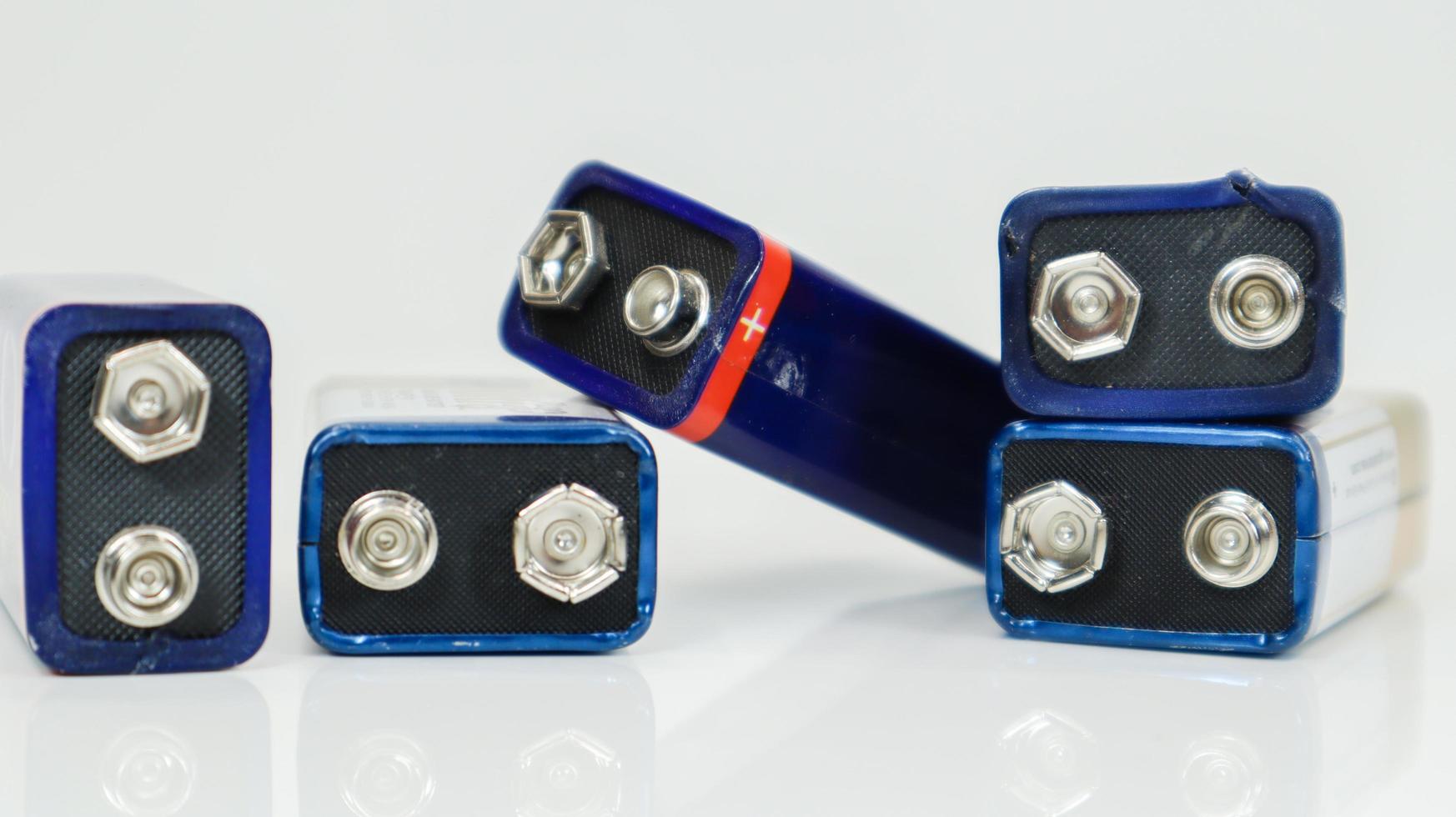 cinq piles pp3 bleues utilisées, disposées de manière chaotique et dispersées sur un fond blanc avec reflet. batterie principale pour les alimentations personnelles. gros plan d'un connecteur de batterie rayé et usé. photo