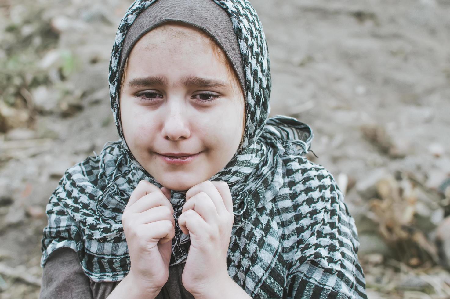 un enfant réfugié dans la guerre, une fille musulmane avec un visage sale sur les ruines, le concept de paix et de guerre, l'enfant pleure et attend de l'aide. photo