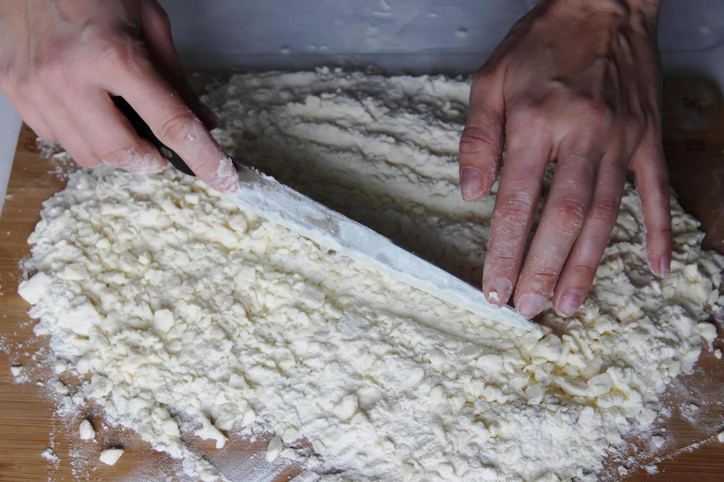 les mains du cuisinier hacher le beurre et la farine sur une planche de bois avec un couteau. gateau maison. travaux ménagers. photo