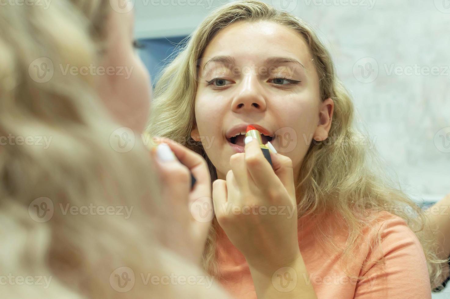 une fille aux cheveux bouclés se peint les lèvres avec du rouge à lèvres rouge devant le miroir à la maison. fermer. mise au point sélective, grain de film. photo