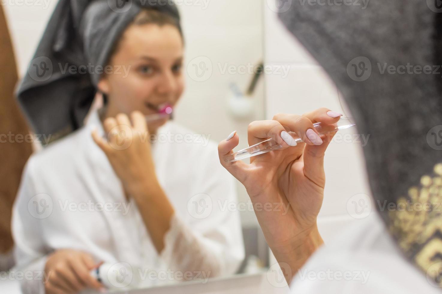 une fille avec une serviette sur la tête se brosse les dents le matin devant un miroir dans la salle de bain. mise au point sélective. grain de film. photo