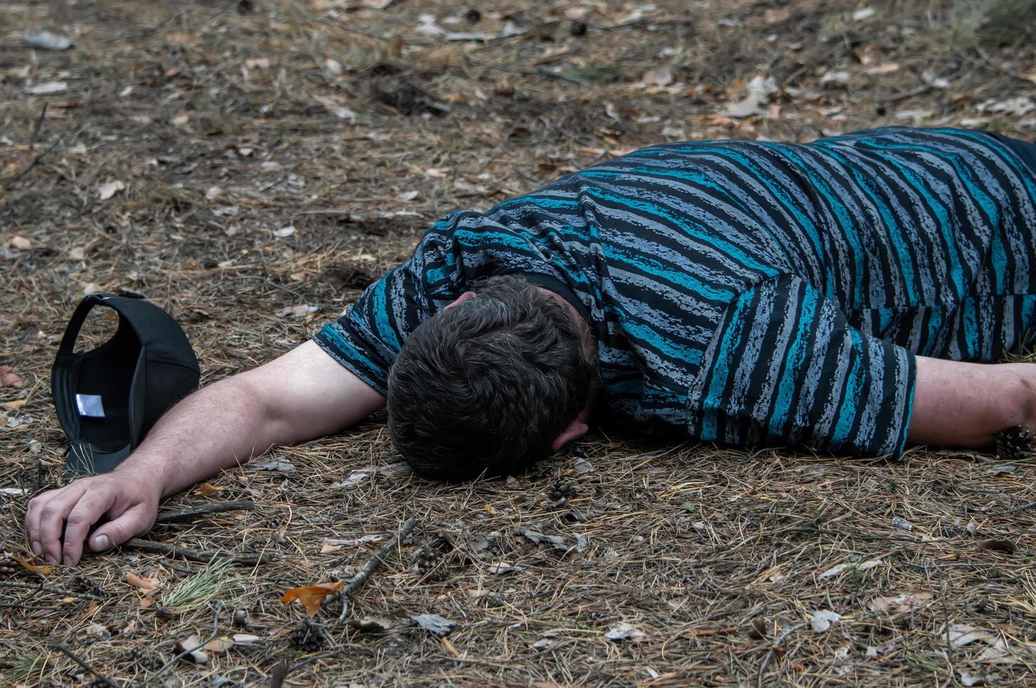 meurtre dans les bois. le corps d'un homme vêtu d'un t-shirt bleu repose sur le sol parmi les arbres de la forêt. victime d'un attentat. photo