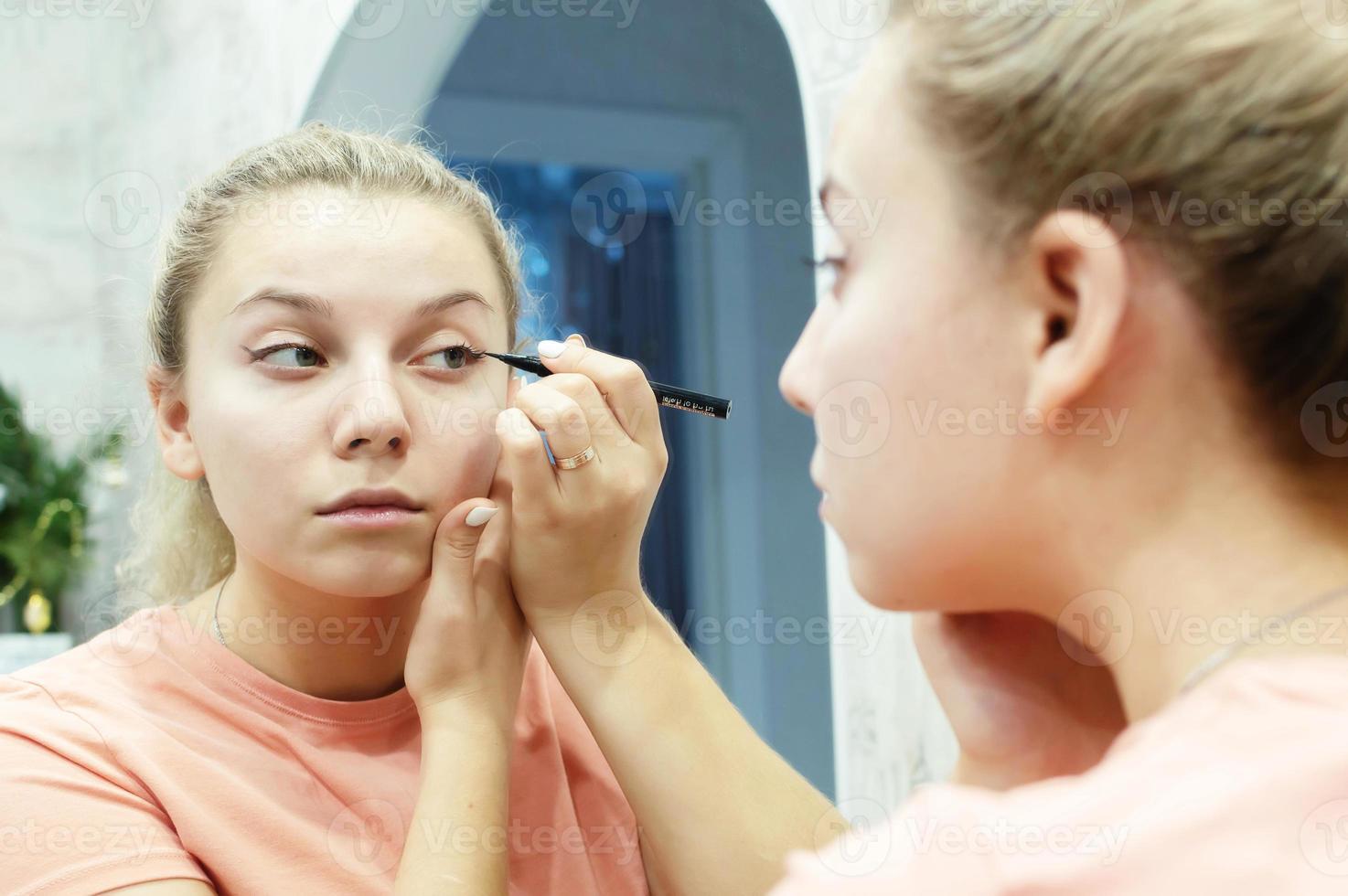 une fille se peint les yeux, fait des flèches à l'aide d'un miroir avant une fête. fermer photo