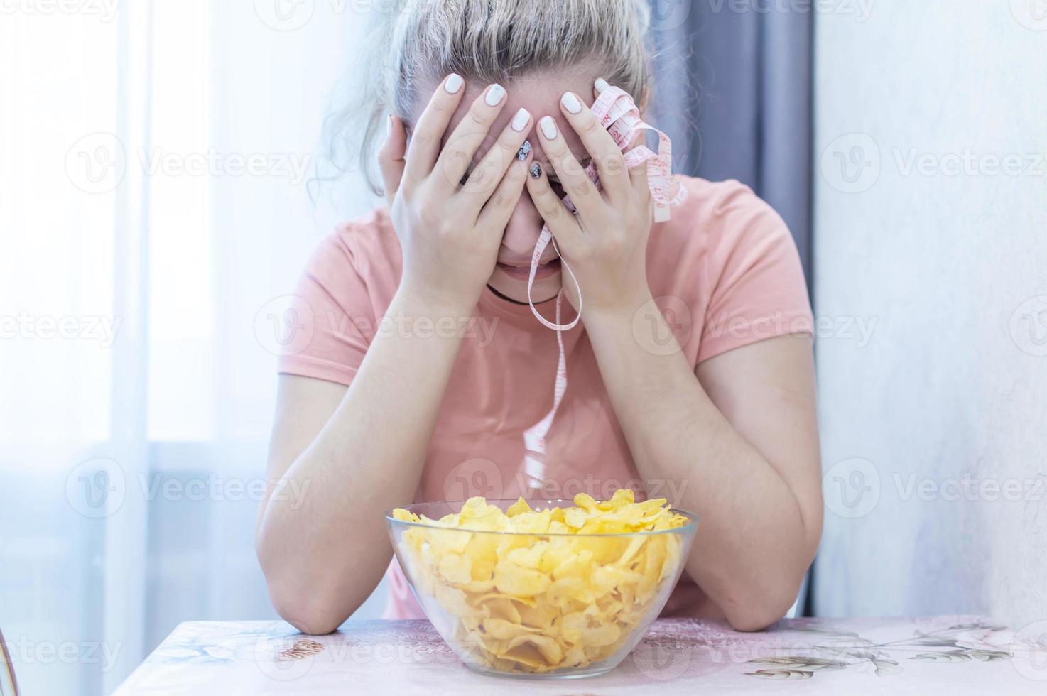 une fille en surpoids pleure, mange des chips et tient un ruban d'un centimètre de long. mal bouffe. mise au point sélective, grain de film. photo