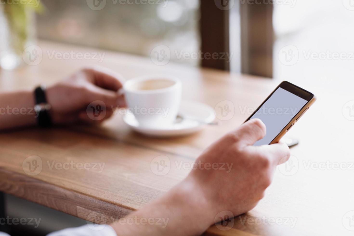 main d'homme d'affaires tenant un téléphone avec écran isolé contre moke et boire du café dans le café fond de tasse de café floue, concept de maquette photo