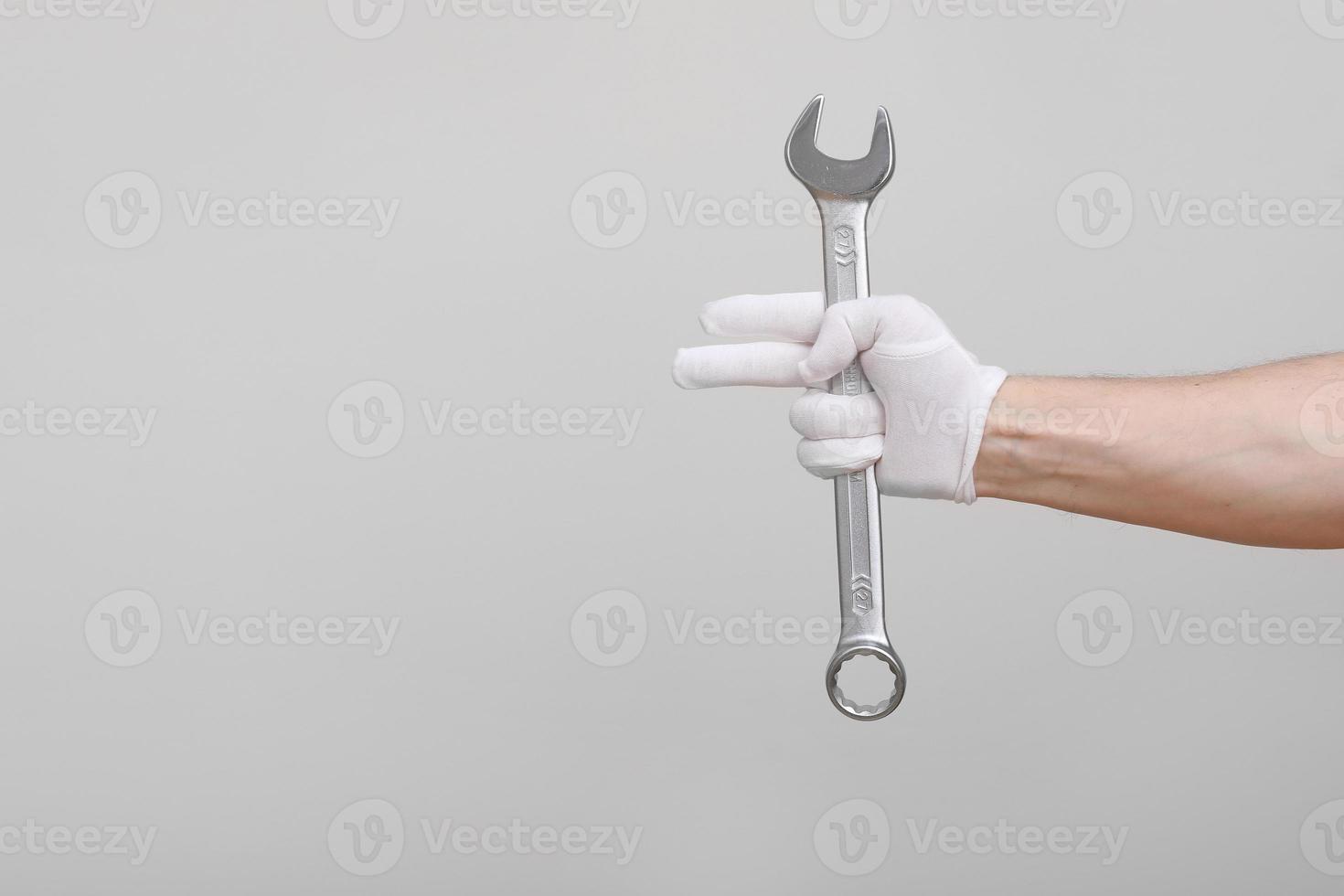 un ouvrier, constructeur, réparateur, bricoleur, mains avec un gant de protection tenant une clé sur fond blanc. maquette de l'espace de copie. photo